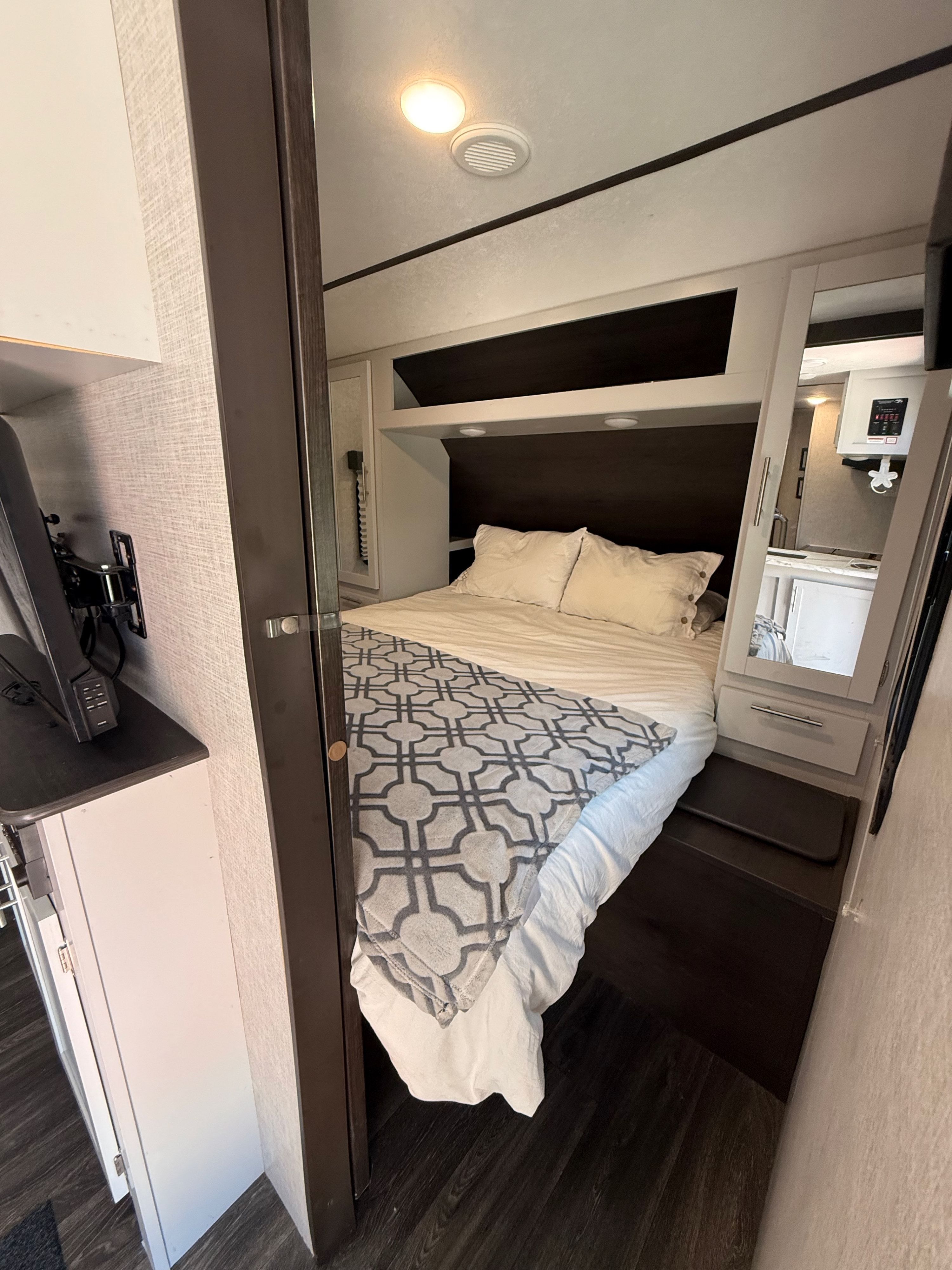 RV rental bedroom with a comfortable bed, patterned throw, overhead storage, and a wall-mounted TV.. Keystone RV Bullet Ultra Lite 2021