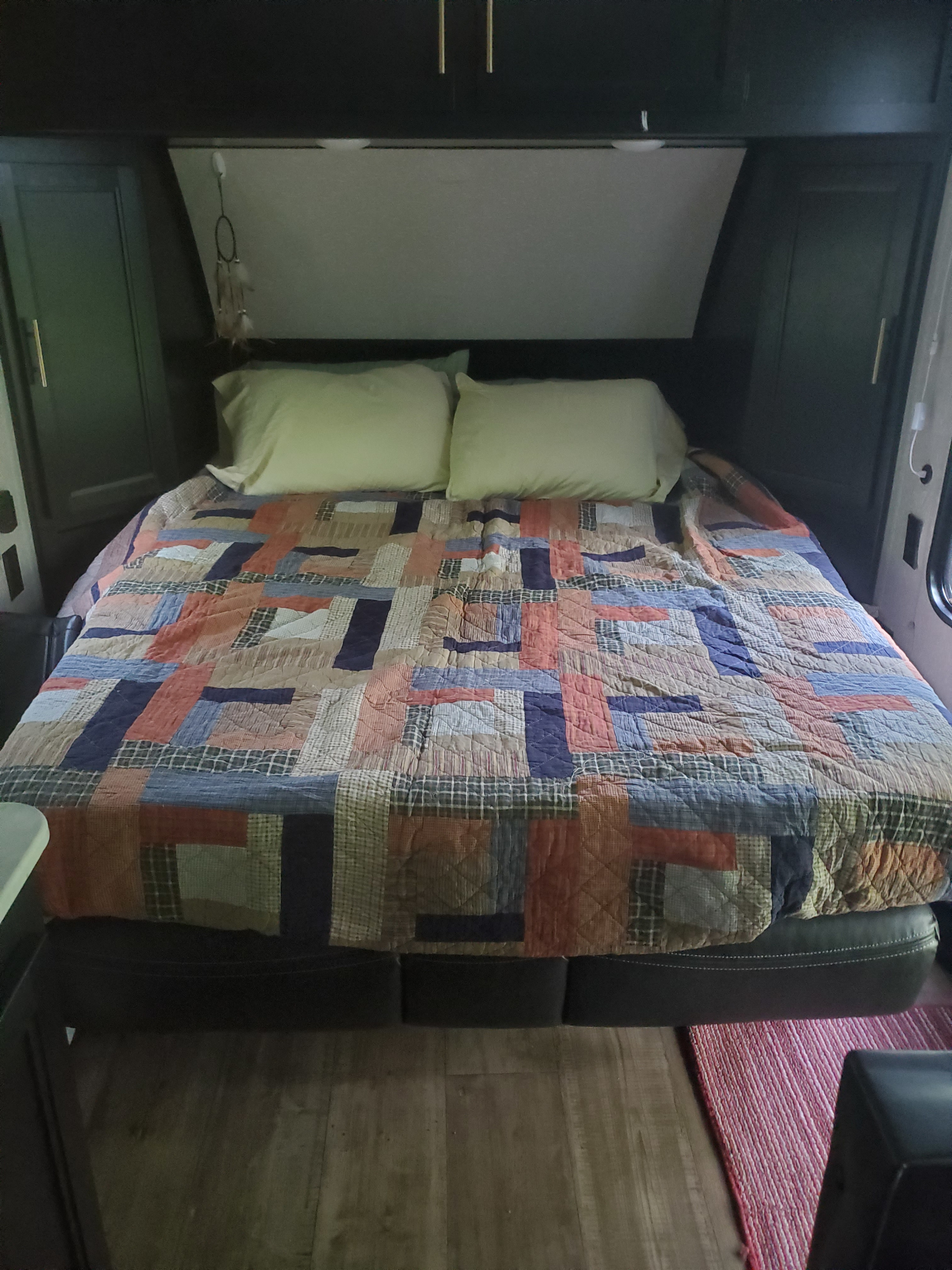 RV rental bedroom: a cozy bed with a colorful patchwork quilt, pillows, and dark built-in storage.. Forest River Cherokee Wolf Pup 2022