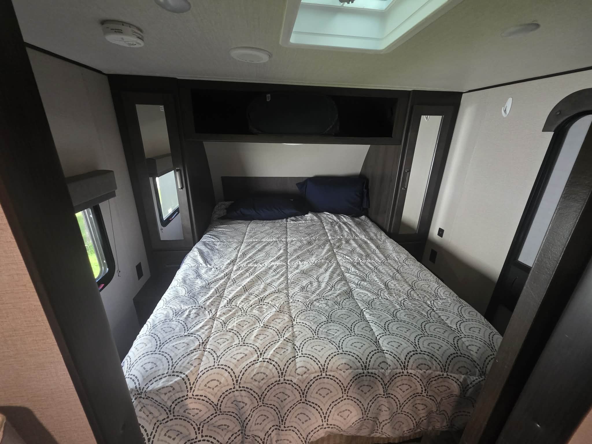 Cozy RV rental bedroom with a comfortable bed, overhead storage, skylight, and windows, ready for your next adventure.. Grand Design Transcend Xplor 2021