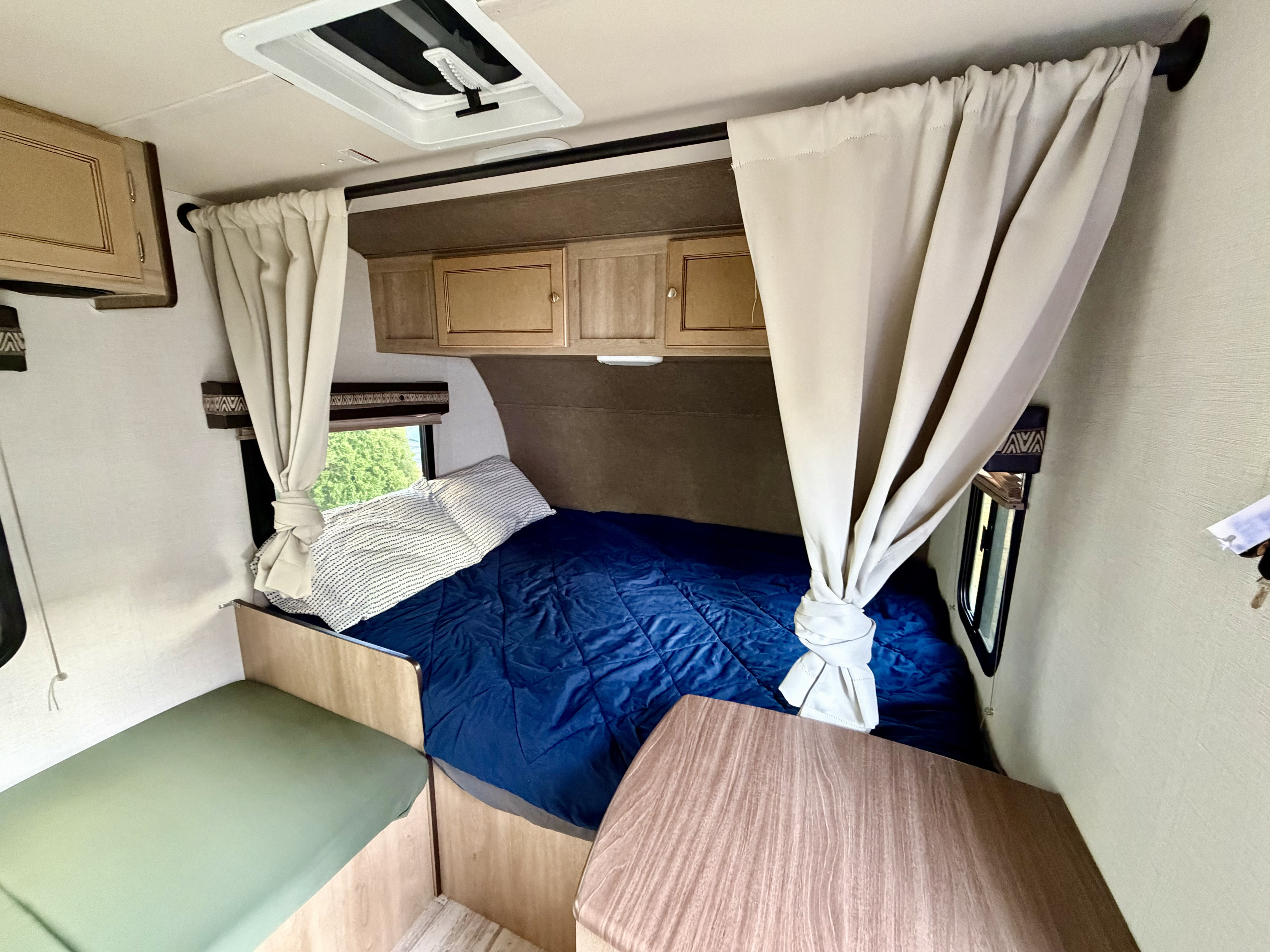 Inside this RV rental: a snug sleeping area with blue bedding, tied curtains, overhead cabinets, and a side dinette.. Palomino Real Lite Mini 2017