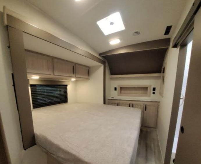 RV rental bedroom with a large bed, overhead cabinets, and a window above. Features a skylight and built-in storage for travel comfort.. Cruiser Rv Corp Stryker 2025