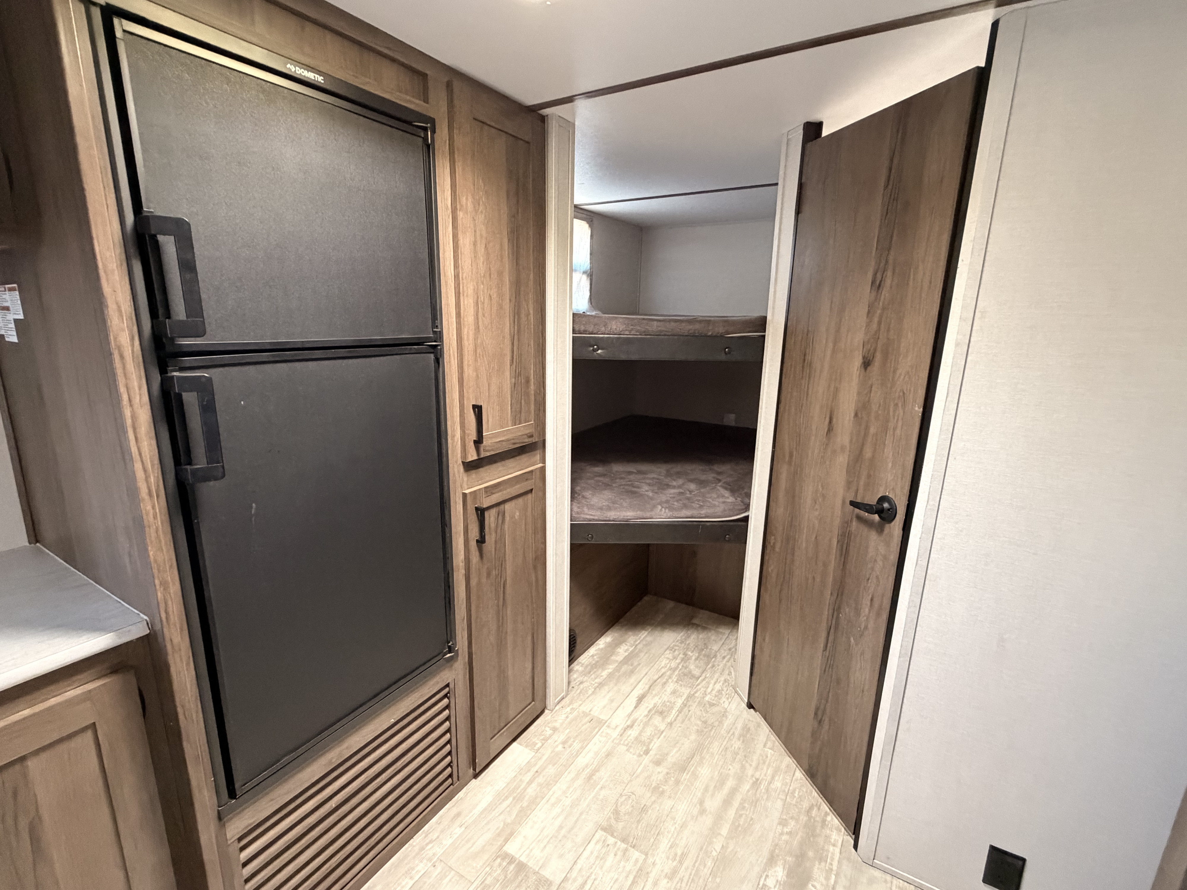This RV rental interior features a black Dometic fridge, wood-tone cabinetry, and cozy bunk beds perfect for travel.. Prime Time Tracer 2020