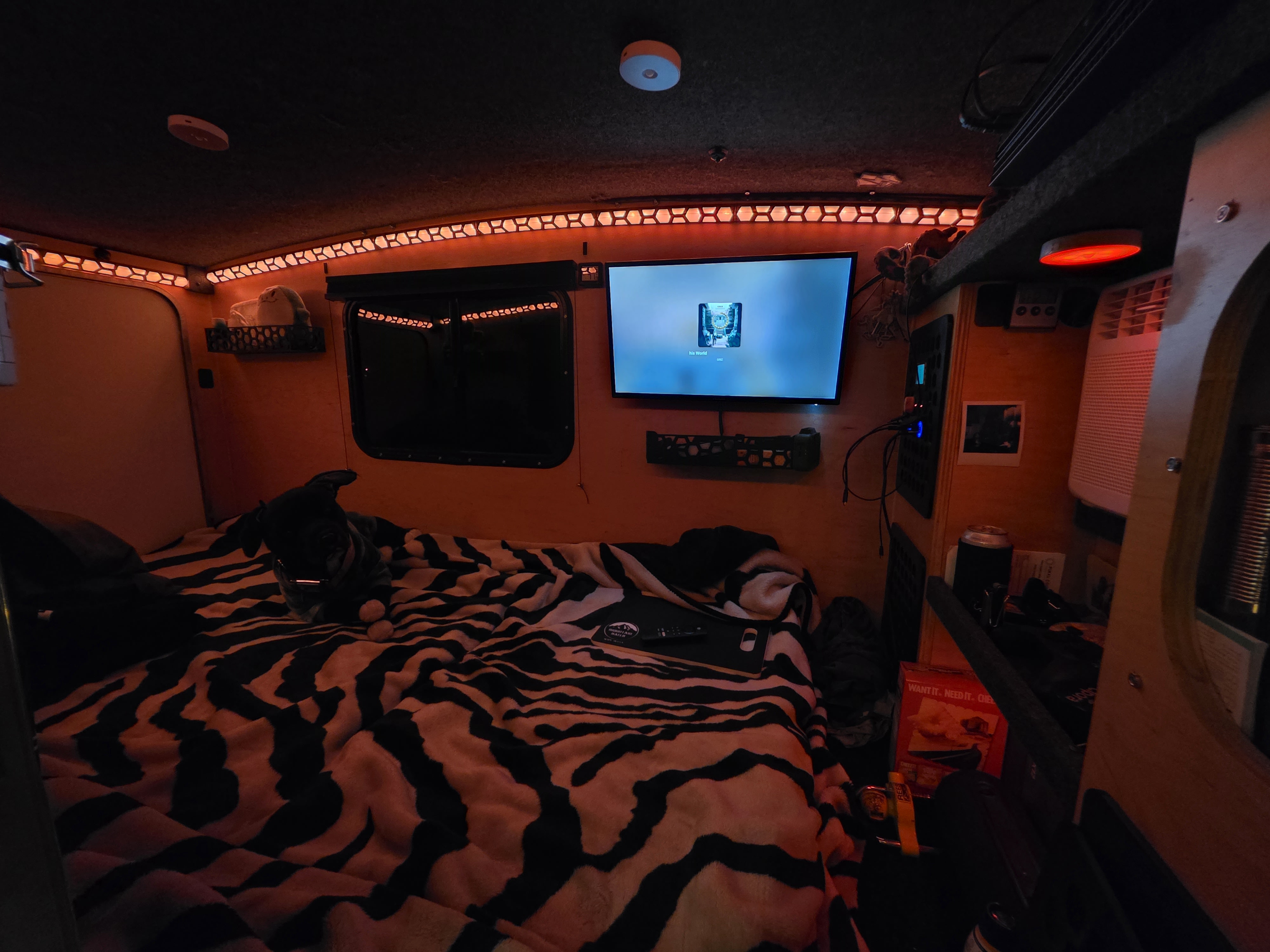 Cozy rv rental interior: dog on a zebra-print bed, TV, and warm red ambient lighting in a compact space.. Runaway Cool Camp 4x8 2018