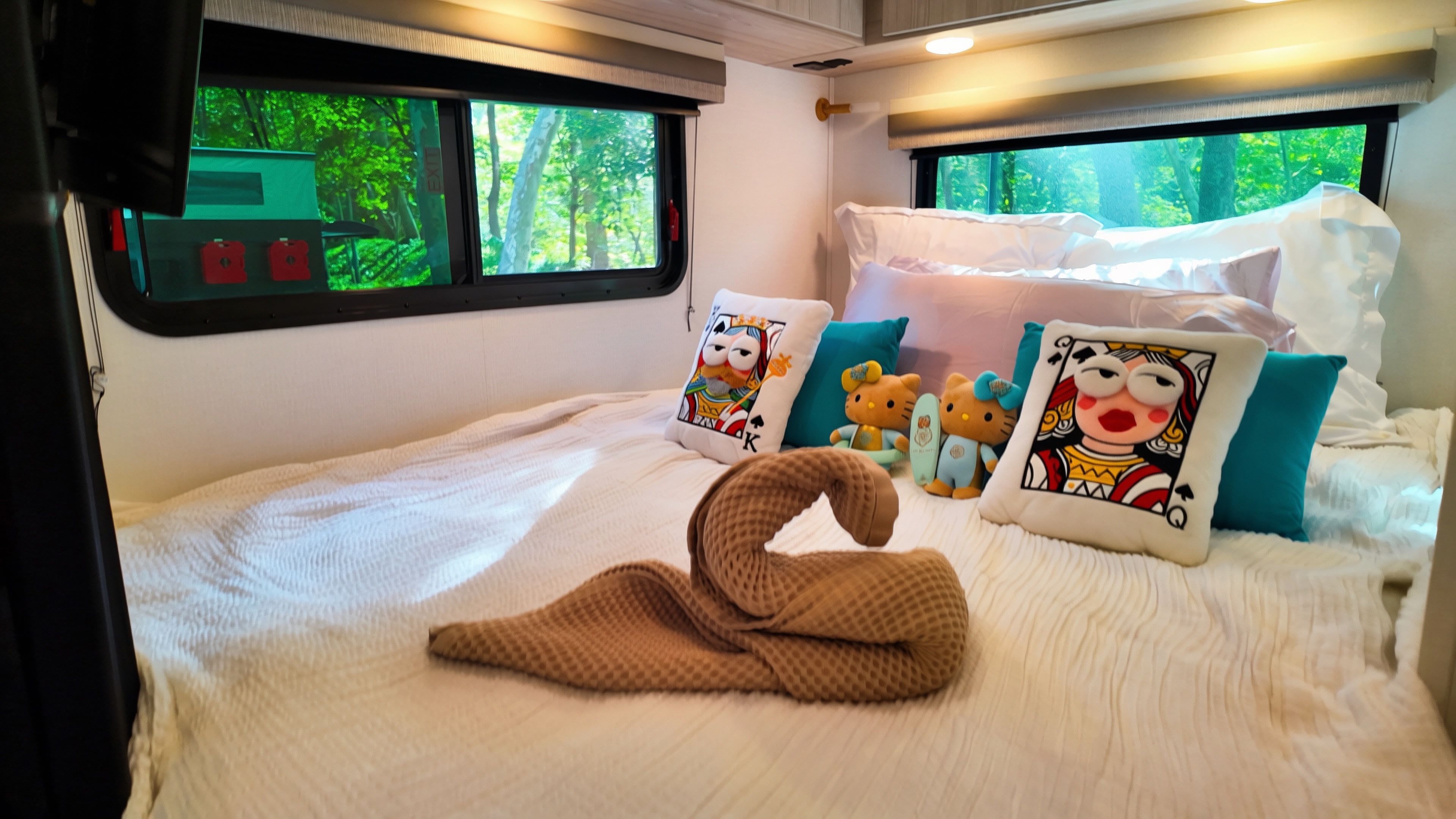 Cozy RV rental bedroom with playful pillows, a towel swan, and lush forest views through the windows. Perfect for glamping adventures.. Forest River Entrada 2026