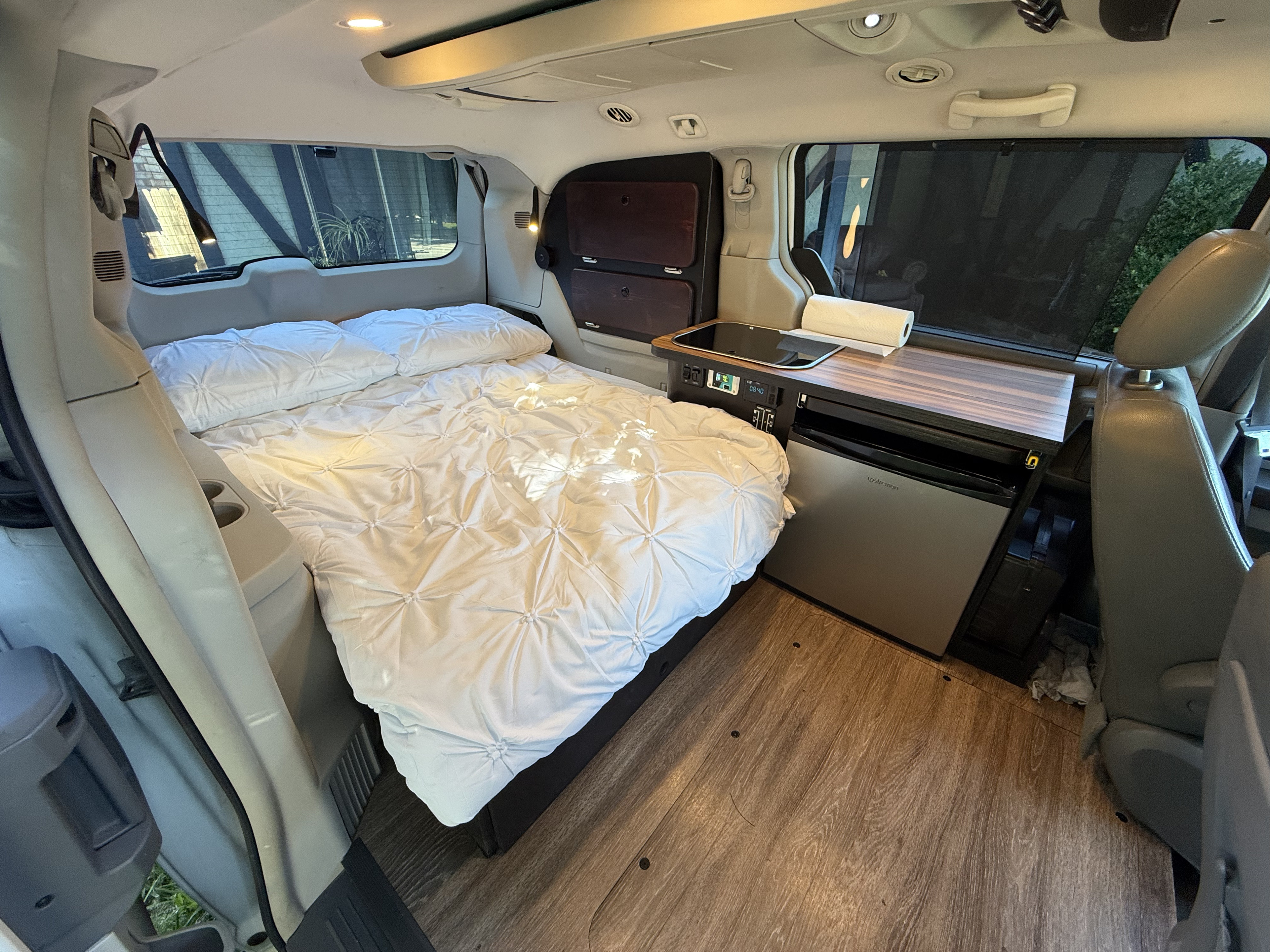 Cozy minivan RV rental interior features a comfy bed, compact kitchen counter with cooktop, and fridge on wooden floor.. Chrysler Town & County 2010