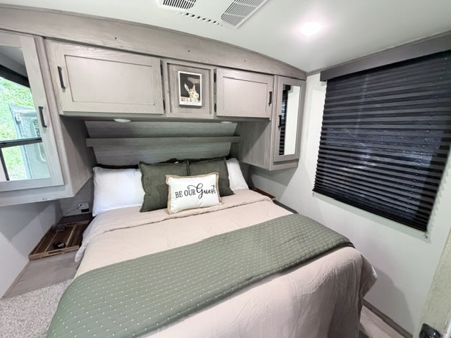 Cozy RV rental bedroom with a comfy bed, sage green accents, and overhead cabinets, offering a welcoming retreat on the road.. Keystone RV Outback Ultra-Lite 2021