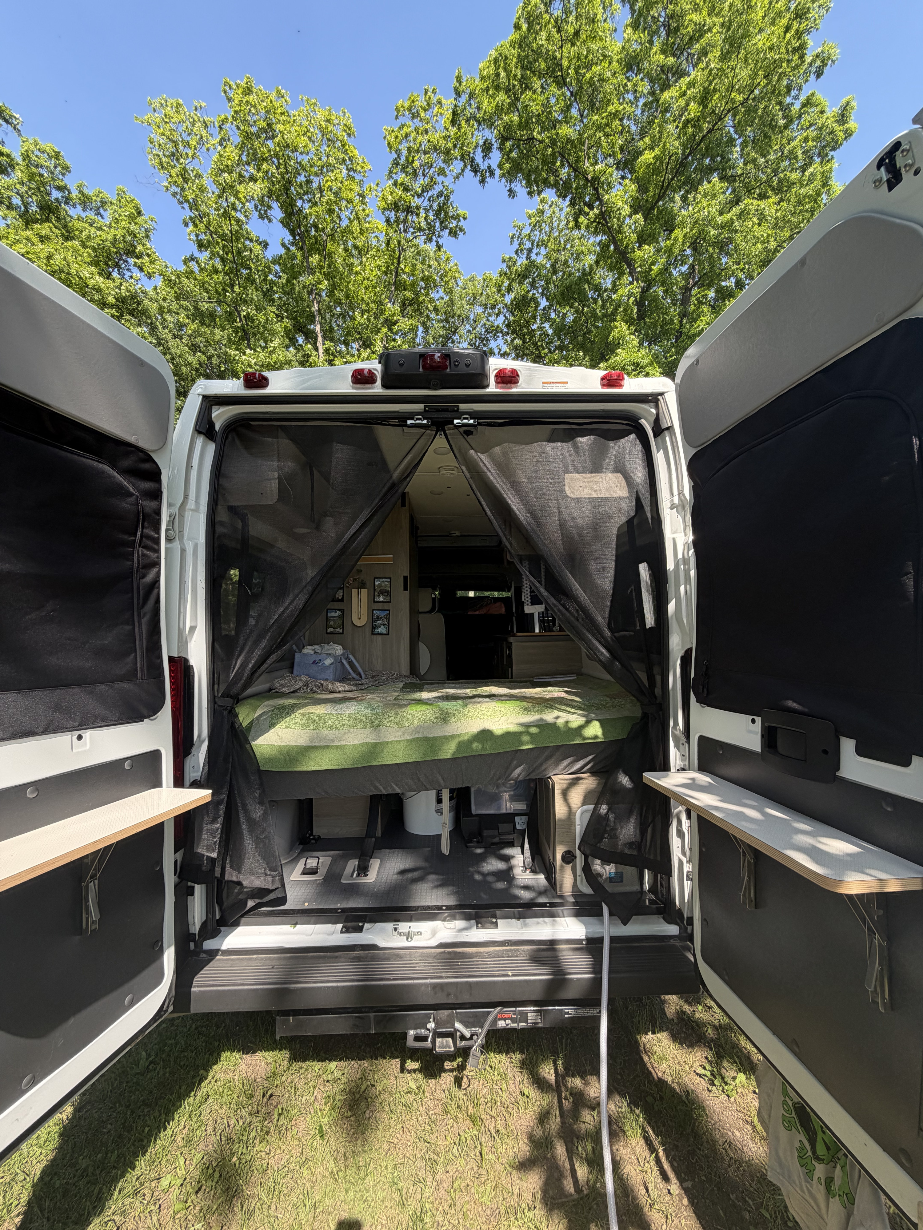 Open rear doors of an RV rental camper van showing its interior bed, mosquito net, and storage, parked outdoors.. Winnebago Solis 2021