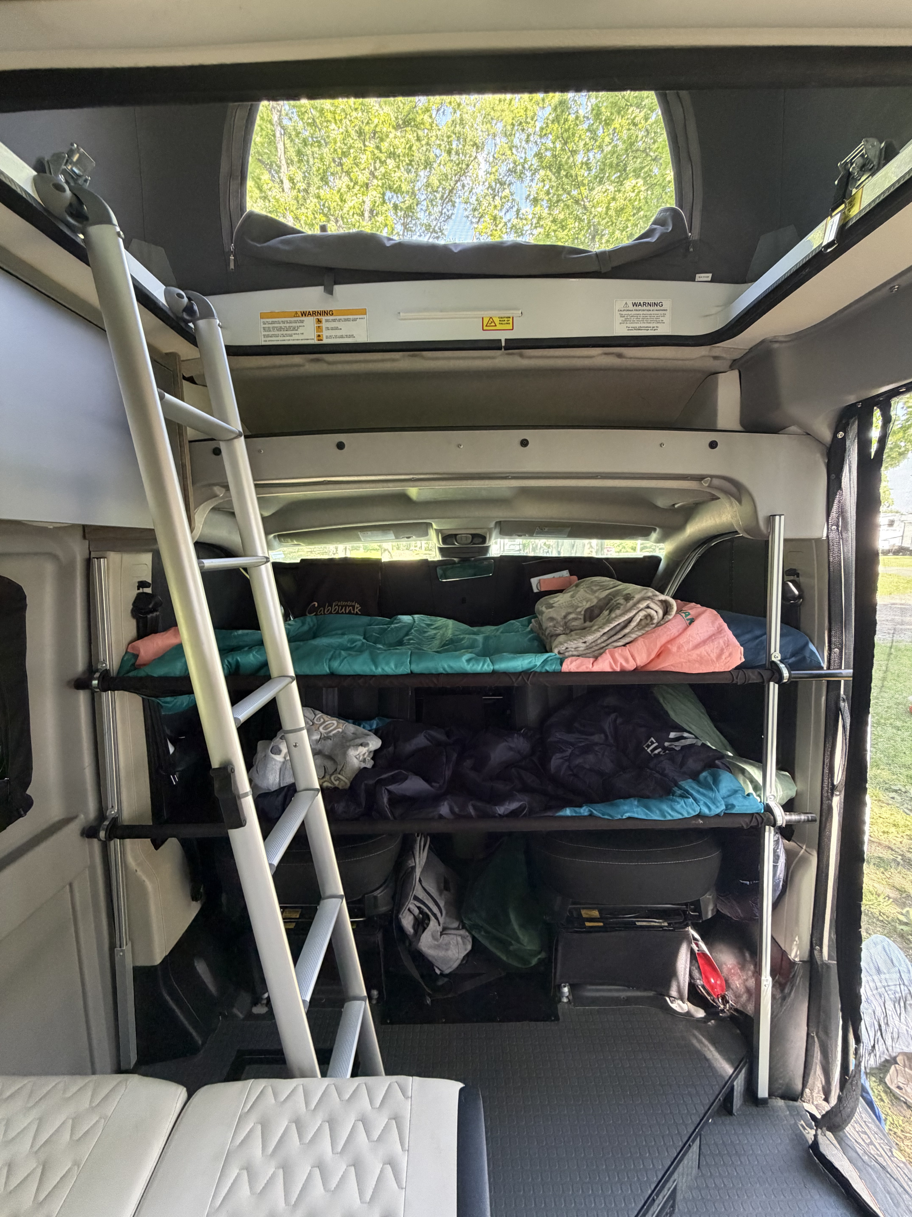 Interior of an RV rental showing stacked bunks, a ladder for access, and a pop-top roof open to trees outside.. Winnebago Solis 2021