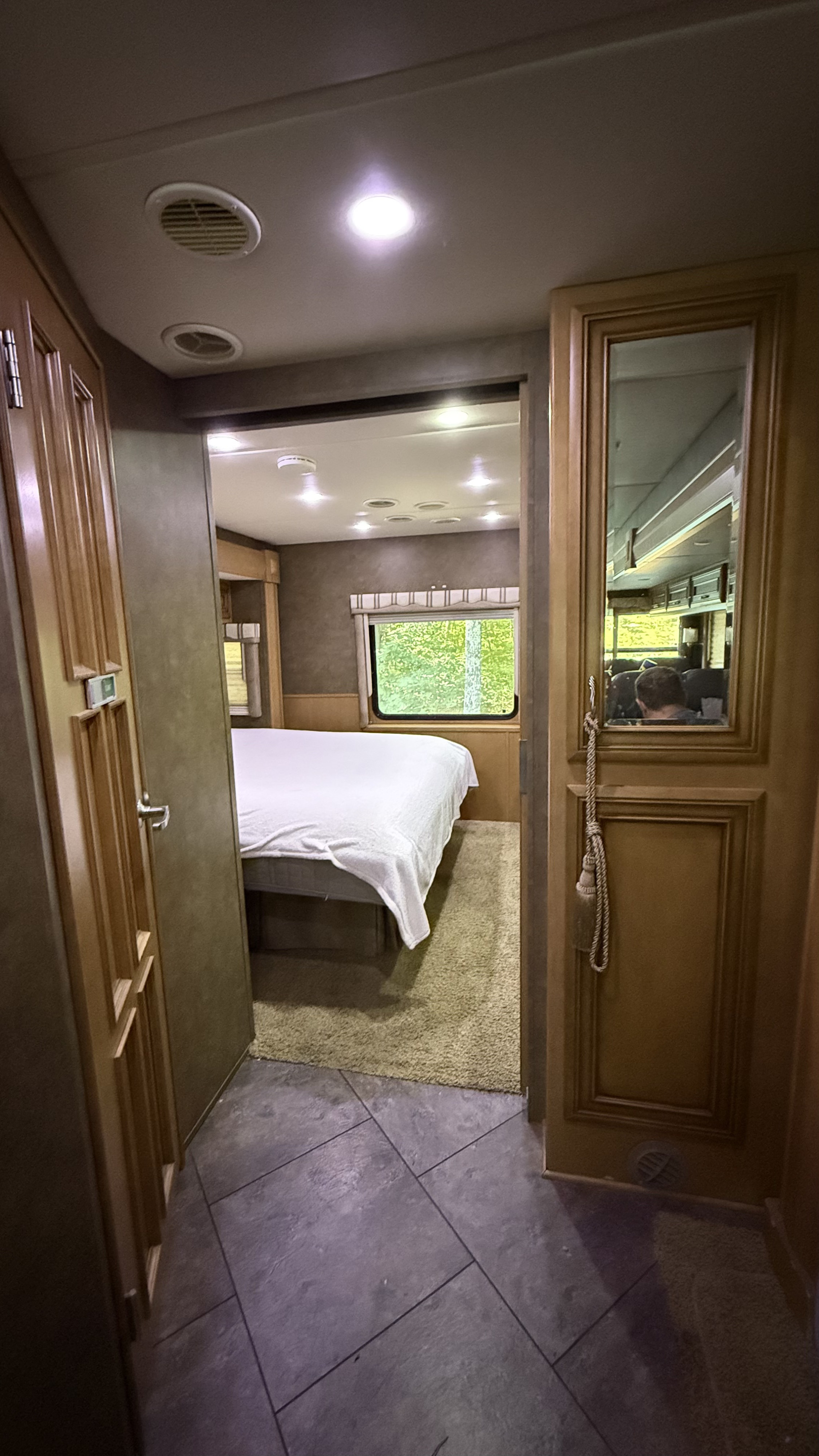 Inside an RV rental: hallway leads to a bedroom with a bed and window, reflected person in mirrored door. Great for travel.. Newmar Baystar 3012 2013