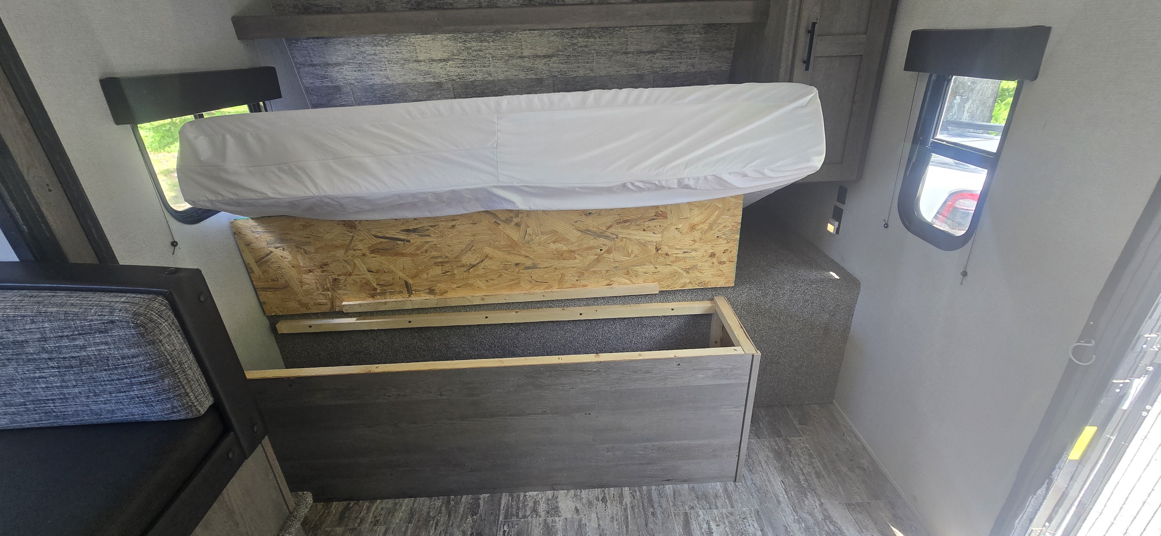 RV rental interior: white mattress on a wood base, with a partially built storage frame visible, next to a window.. Keystone RV Springdale 2019