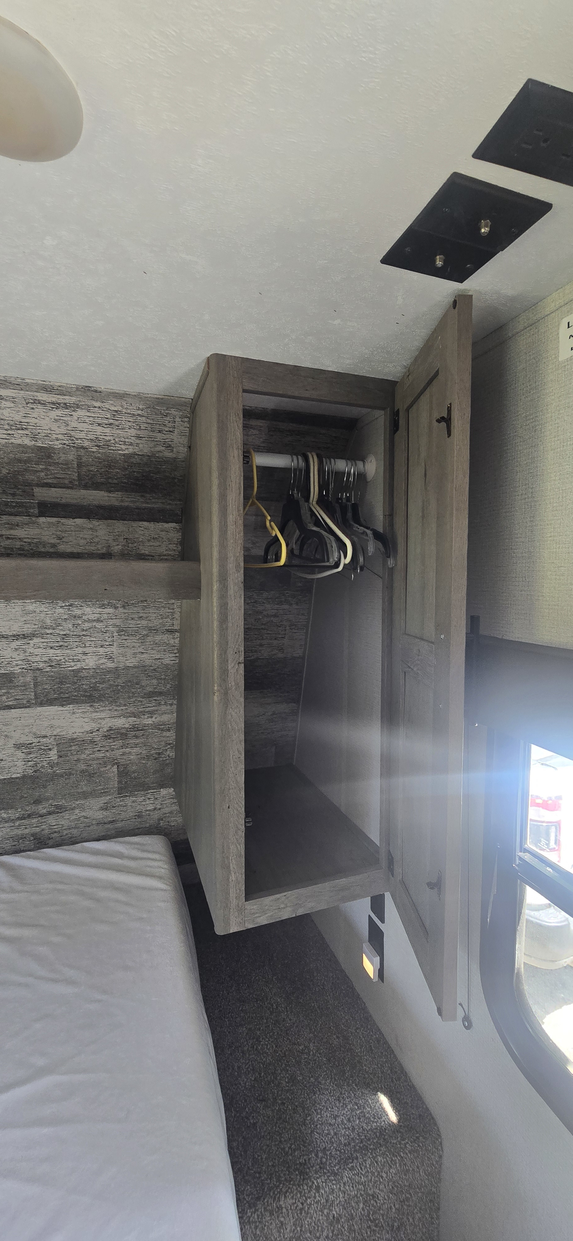 This RV rental bedroom features a hanging wardrobe above the bed, providing convenient storage. Natural light streams from the window.. Keystone RV Springdale 2019