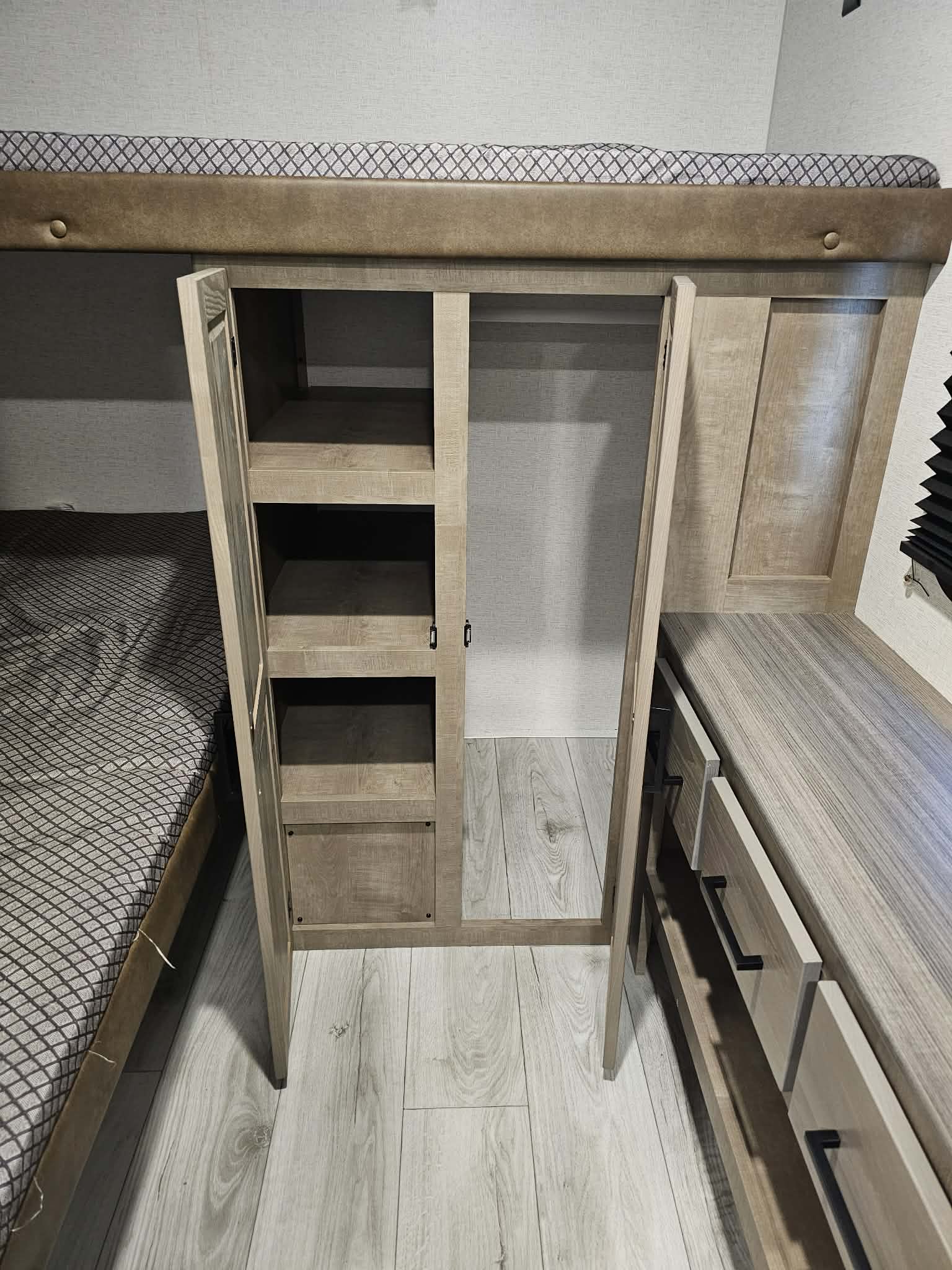 An RV rental interior showing a bunk bed, open wood-toned closet with shelves, and a dresser, maximizing small space.. Keystone RV springdale 2025