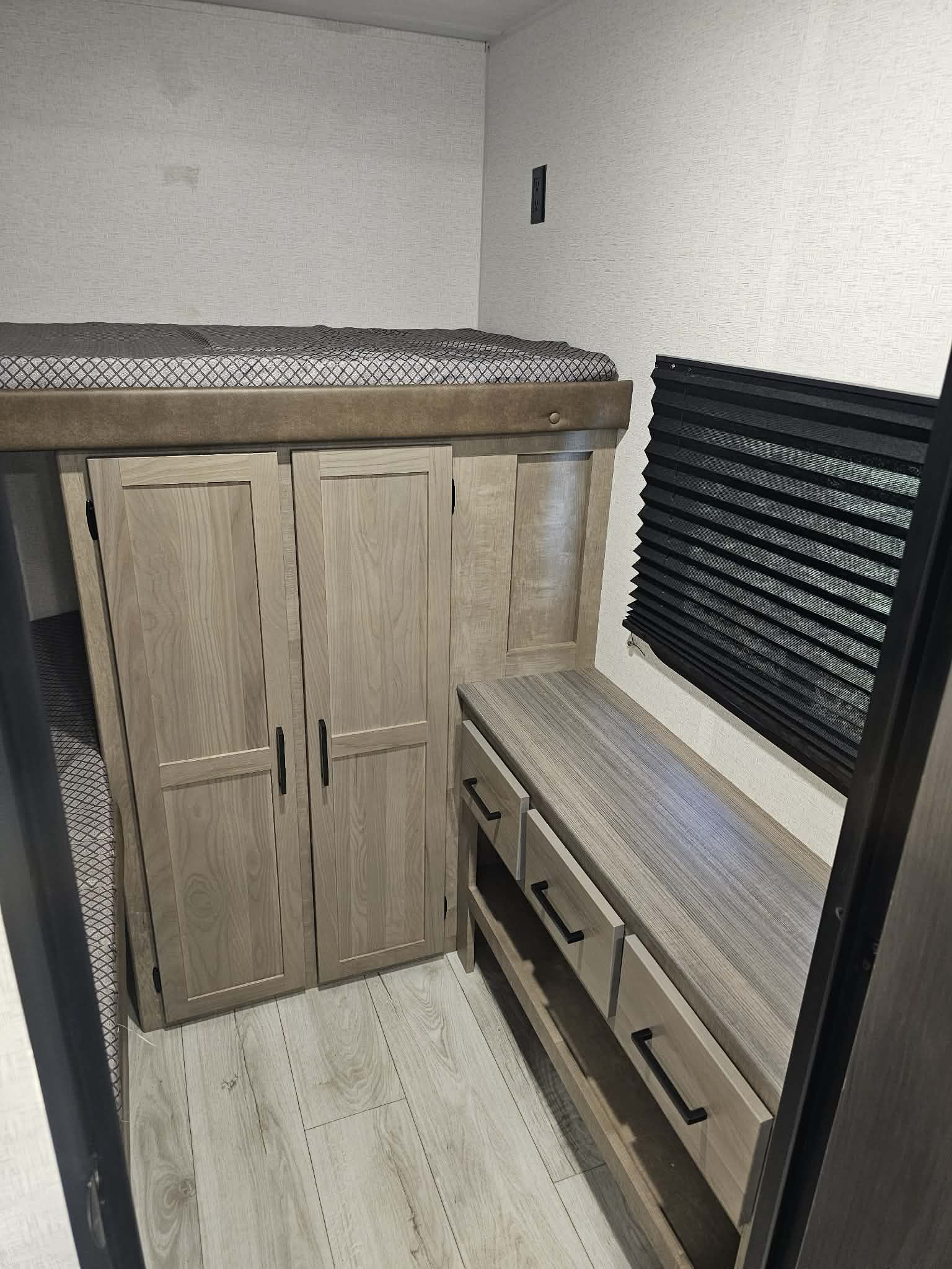 This RV rental interior features bunk beds, light wood storage cabinets and drawers, and a dark pleated window blind.. Keystone RV springdale 2025