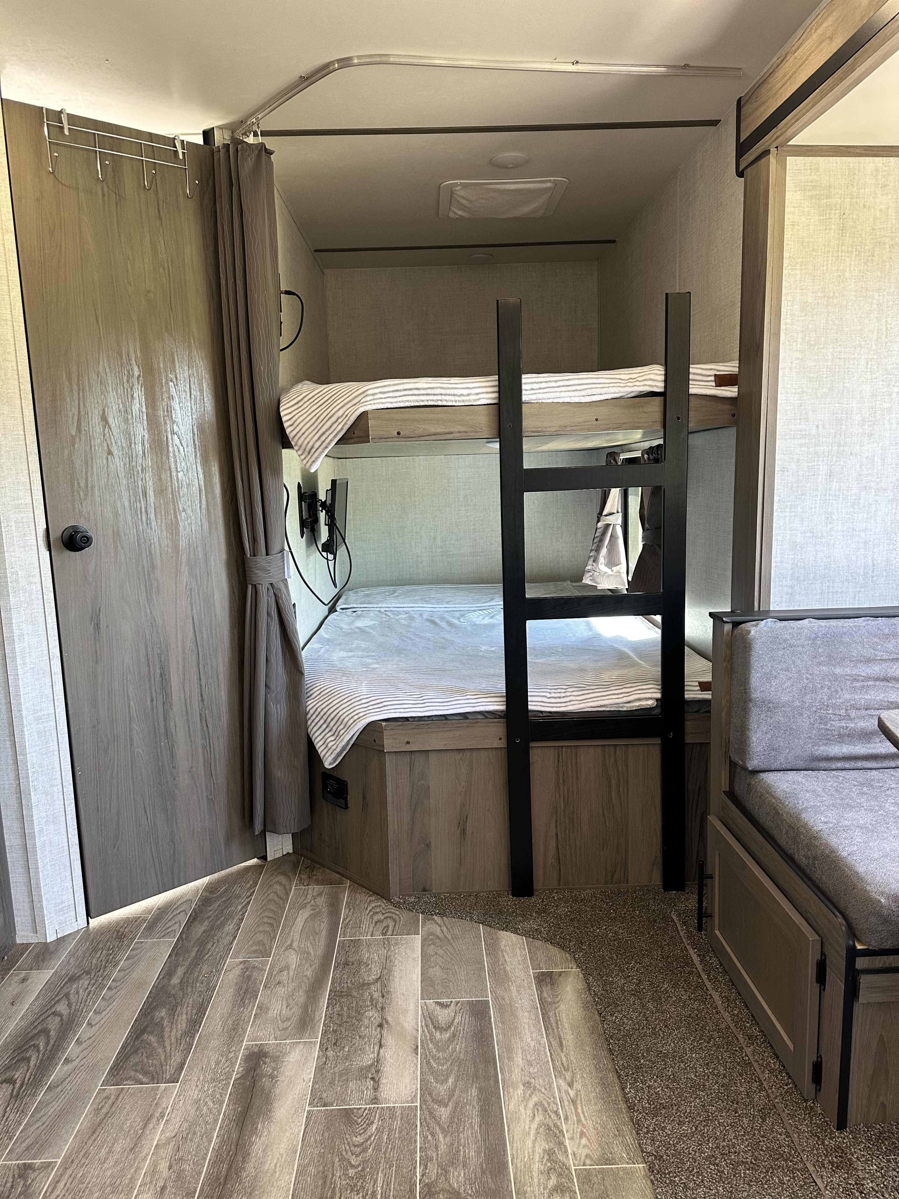 Inside an RV rental, showing bunk beds with striped blankets, a ladder, and a gray dinette. Wood-look flooring transitions to carpet.. Gulf Stream Ameri-Lite 2021
