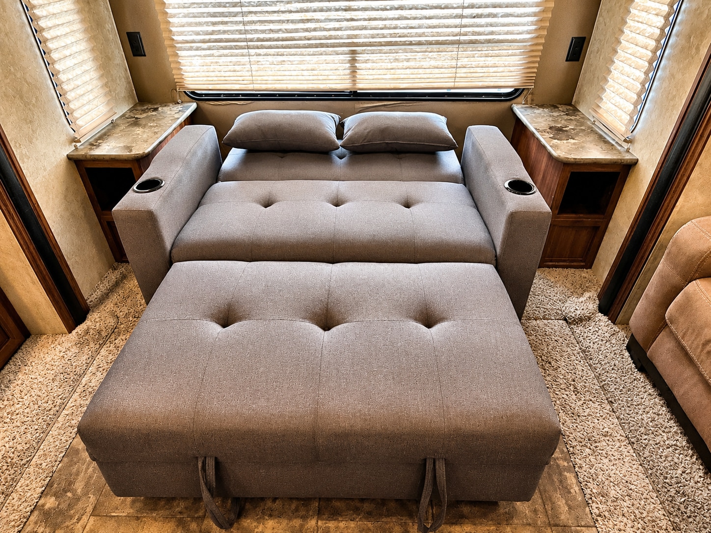 Comfortable RV rental pull-out sofa bed in gray fabric, featuring cupholders and side tables. Perfect for relaxation.. Keystone RV Cougar 2014
