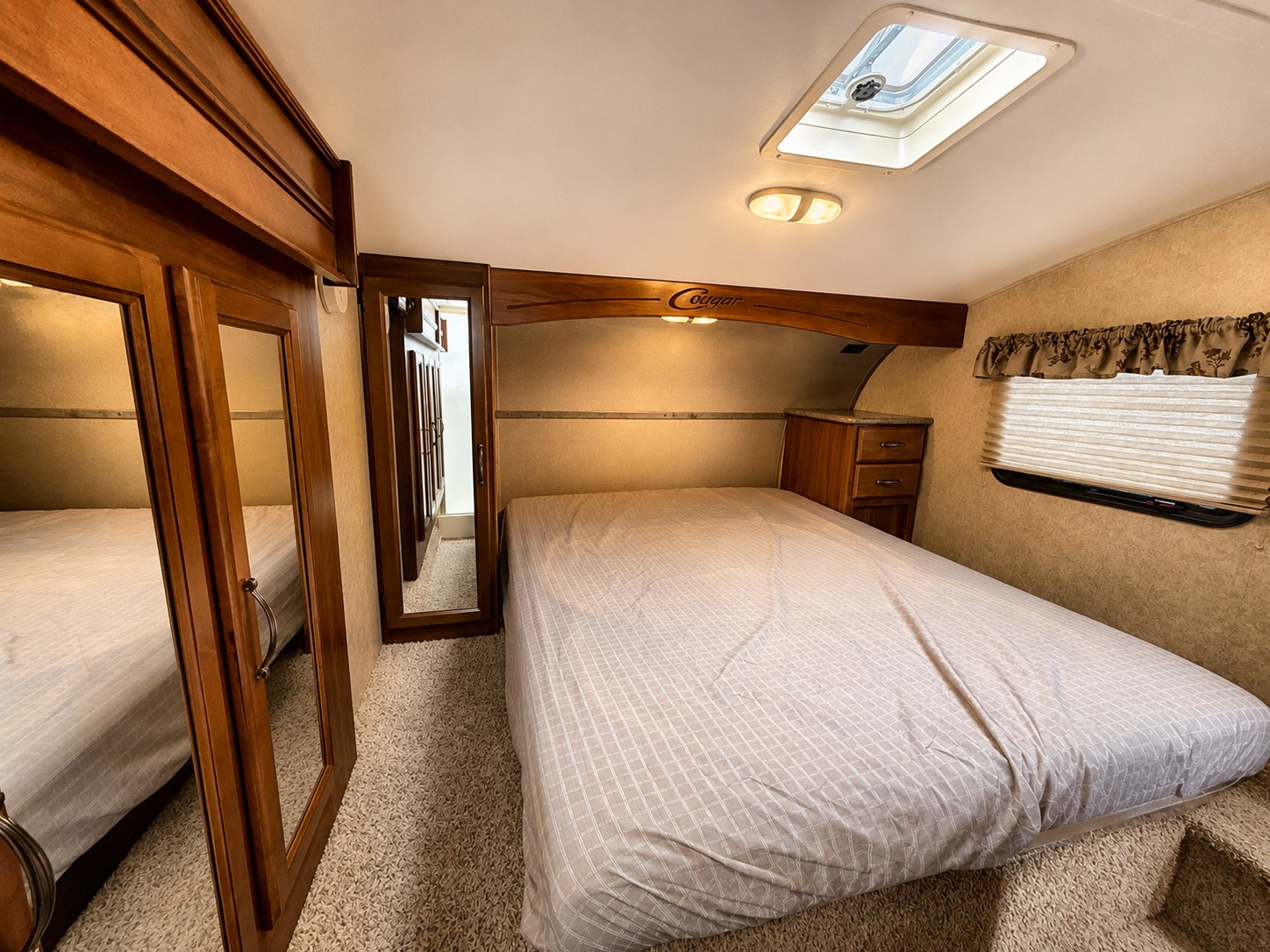 RV rental interior: cozy bedroom with a comfortable bed, skylight, and wood cabinets. Mirrored closets enhance space.. Keystone RV Cougar 2014