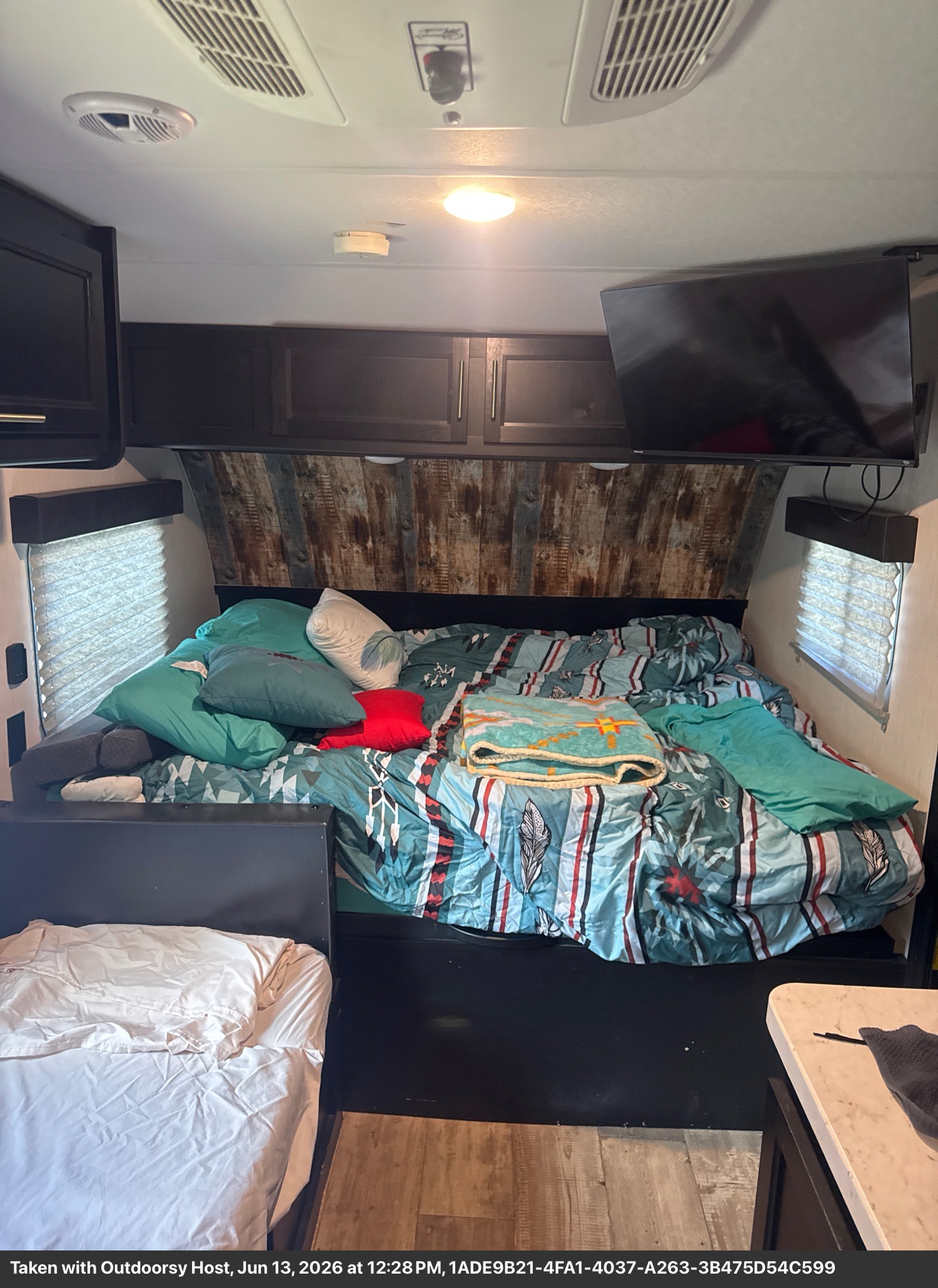 RV rental bedroom featuring a main bed with colorful bedding & pillows, a second bed, TV, and wooden accents.. Forest River Cherokee Wolf Pup 2022