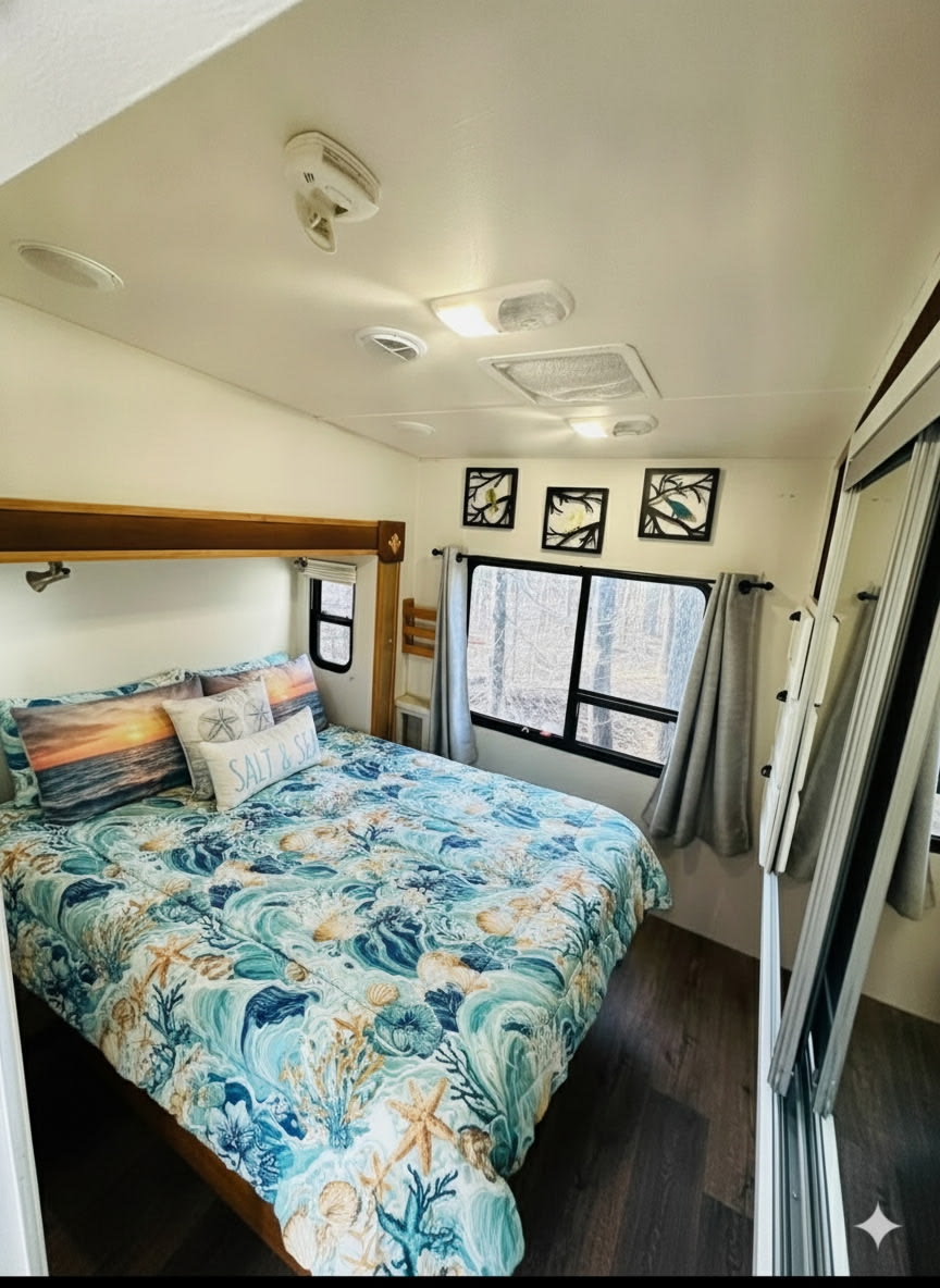 Cozy RV rental bedroom with an ocean-themed comforter and pillows, a window revealing forest trees, and a mirrored closet.. Forest River Wildcat 2008