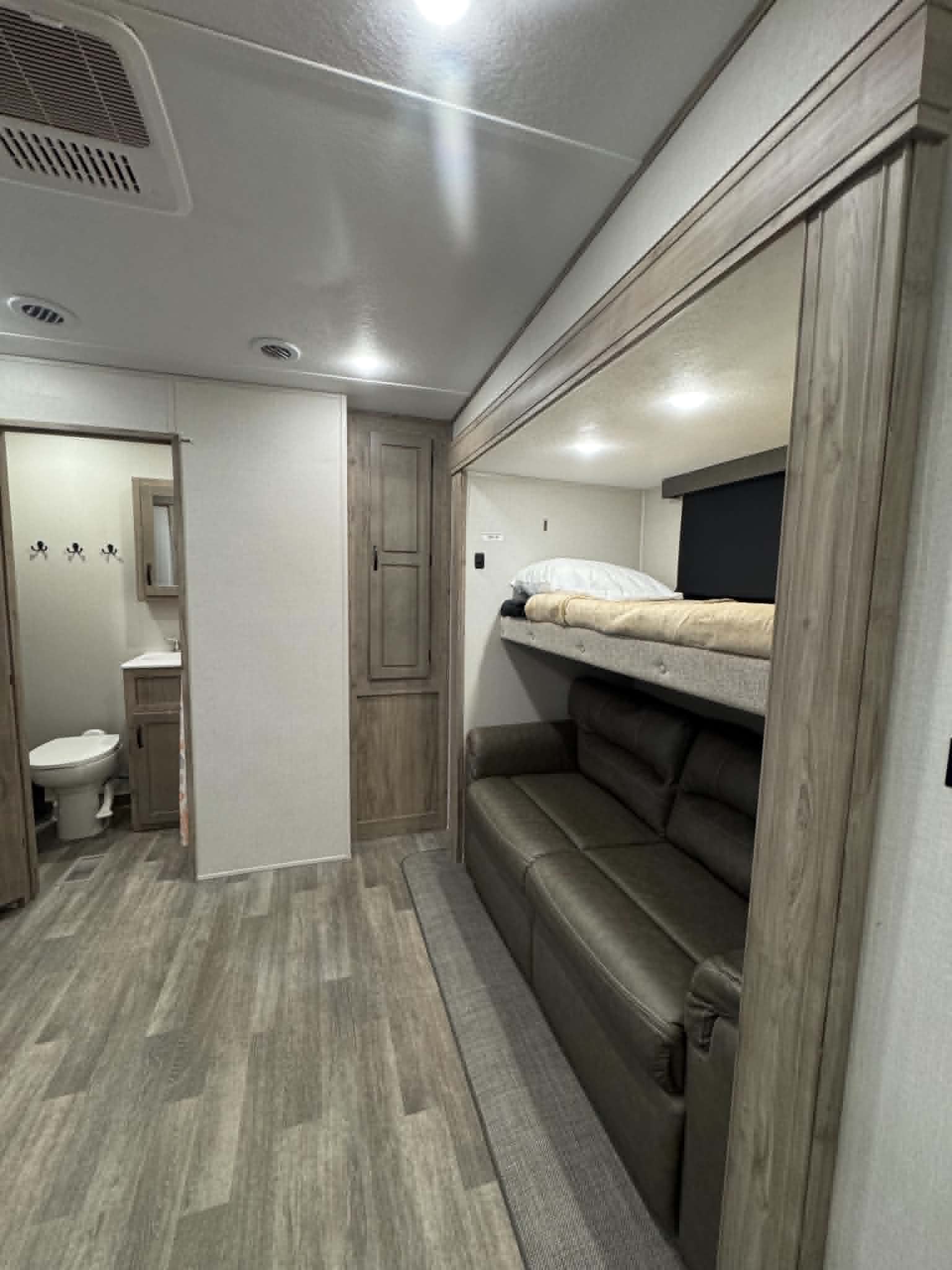 RV rental interior: bunk bed above a sofa, wood-look flooring, and a visible bathroom entrance.. Forest River Coachmen Chaparral 2023