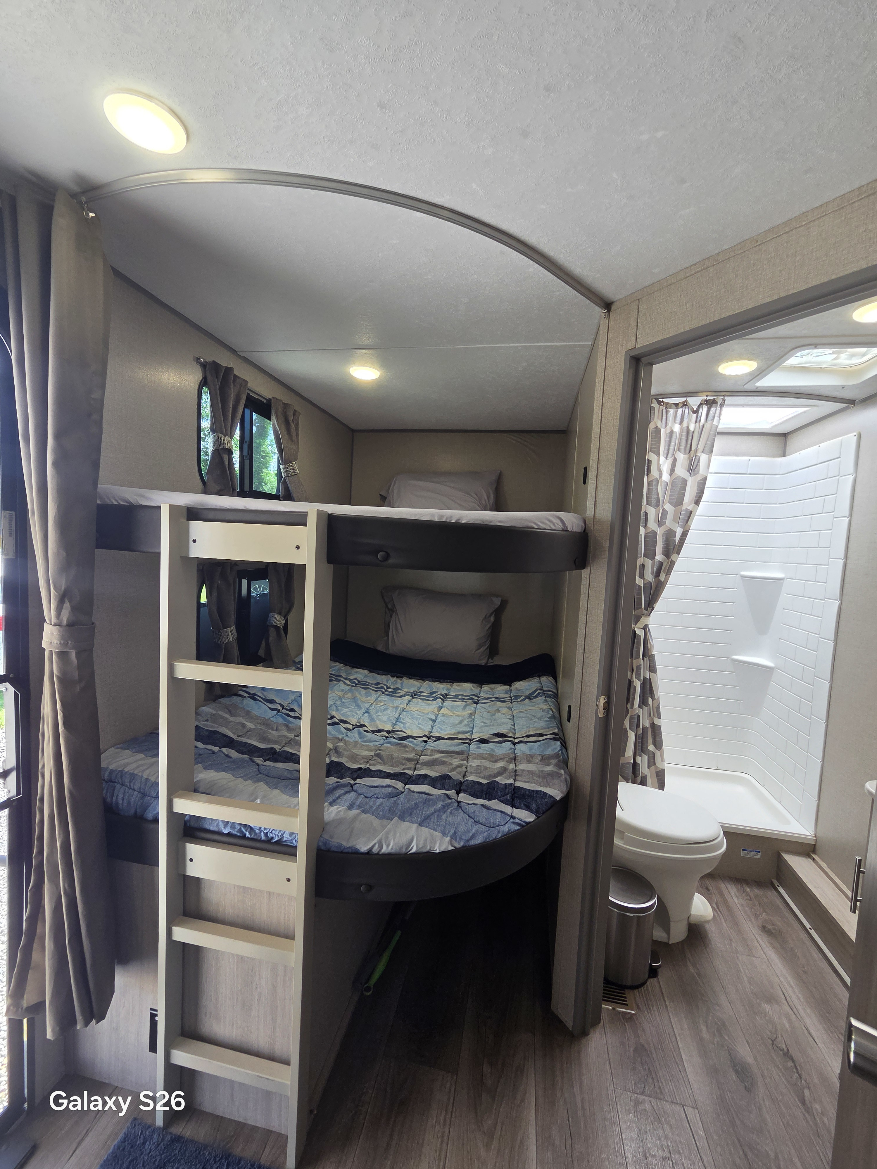 Inside an RV rental: cozy bunk beds with ladder and a compact bathroom featuring a toilet and shower.. Forest River Coachmen Catalina Legacy 2023