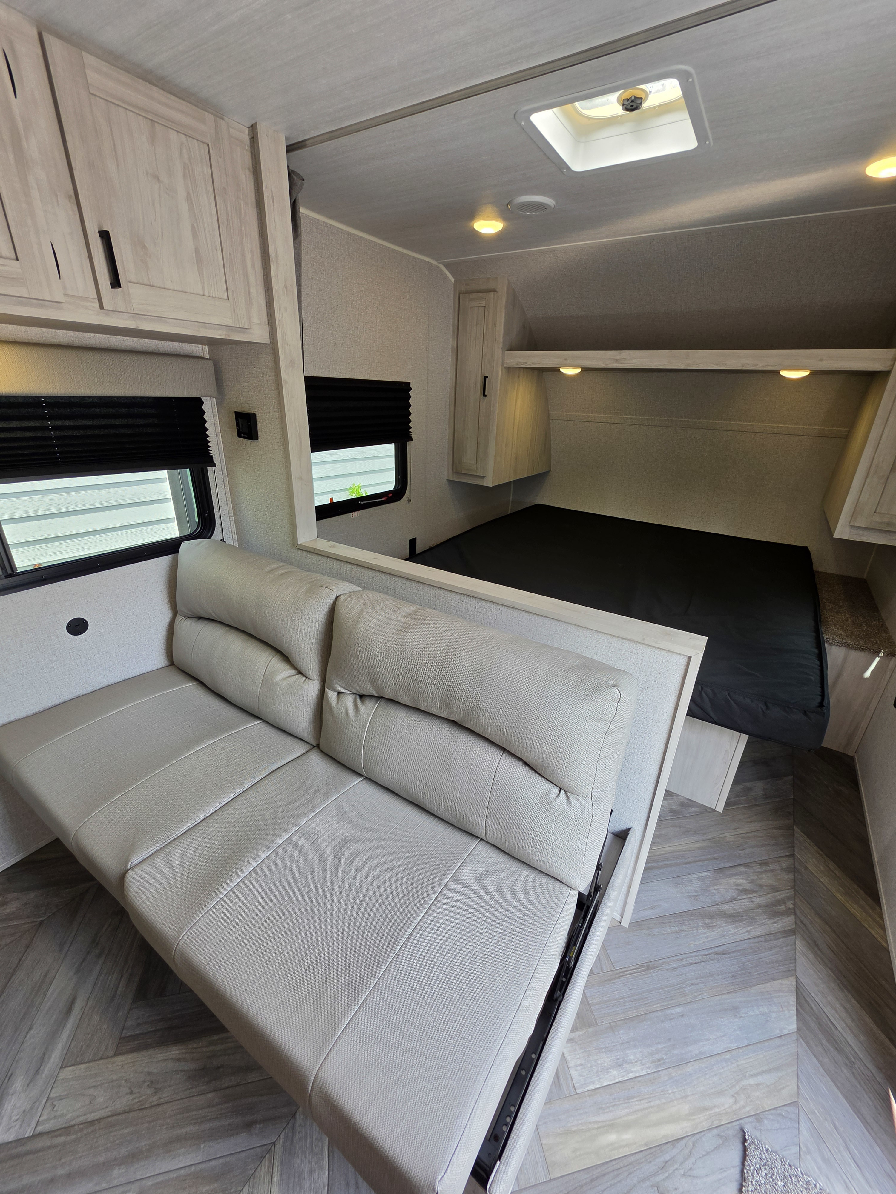Modern RV rental interior with a light-toned convertible sofa, bed area, and sleek wood-look cabinetry for your travels.. East to West Della Terra LE 2024