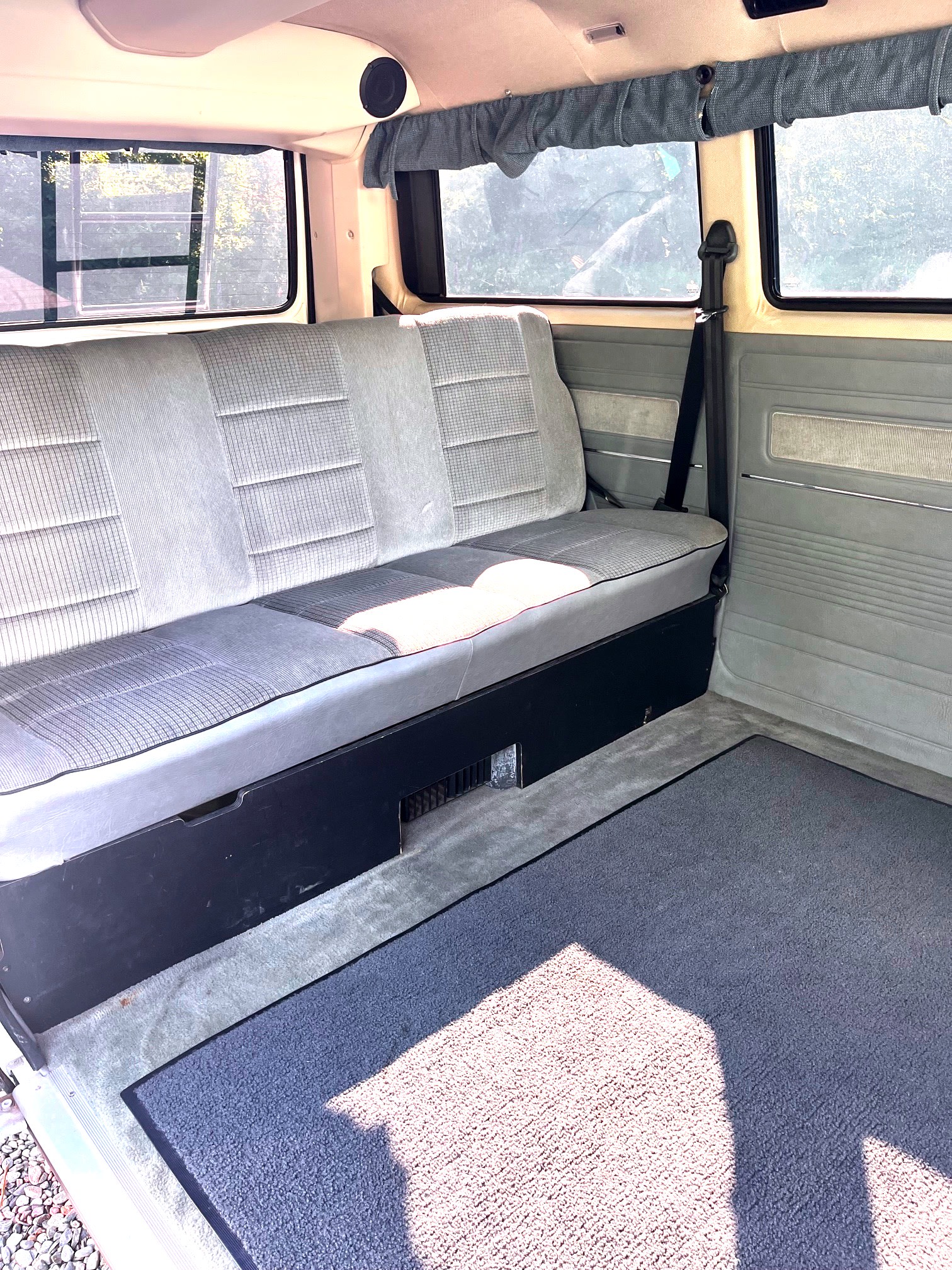 Step inside this RV rental! Rear interior with a patterned bench seat, windows, and carpeted floor for comfortable travel.. Volkswagen Vanagon 1990