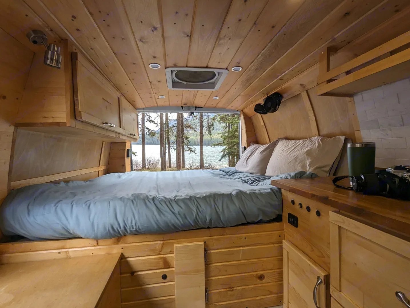 Inside a cozy RV rental: custom wood interior, comfortable bed, and a stunning lake view. Ideal for van life adventures!. Gmc Savanna 2500 2016