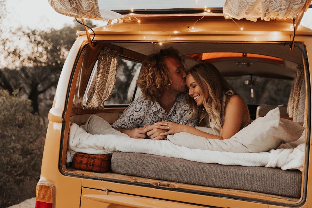 Cozy rv rental romance: A smiling couple shares a tender kiss in the back of their vintage campervan, surrounded by comfort.. Volkswagen Westfalia 1972