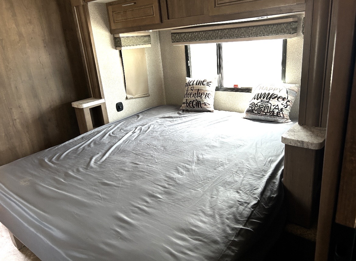 RV rental bedroom with a spacious bed, "Happy Campers" pillows, windows, and overhead storage for comfortable travel.. Forest River Georgetown 2019