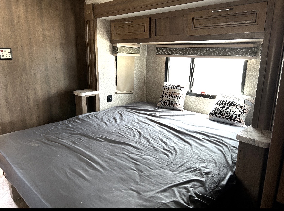 Experience comfort in this RV rental bedroom: a bed with gray sheets, decorative pillows, and storage cabinets.. Forest River Georgetown 2019
