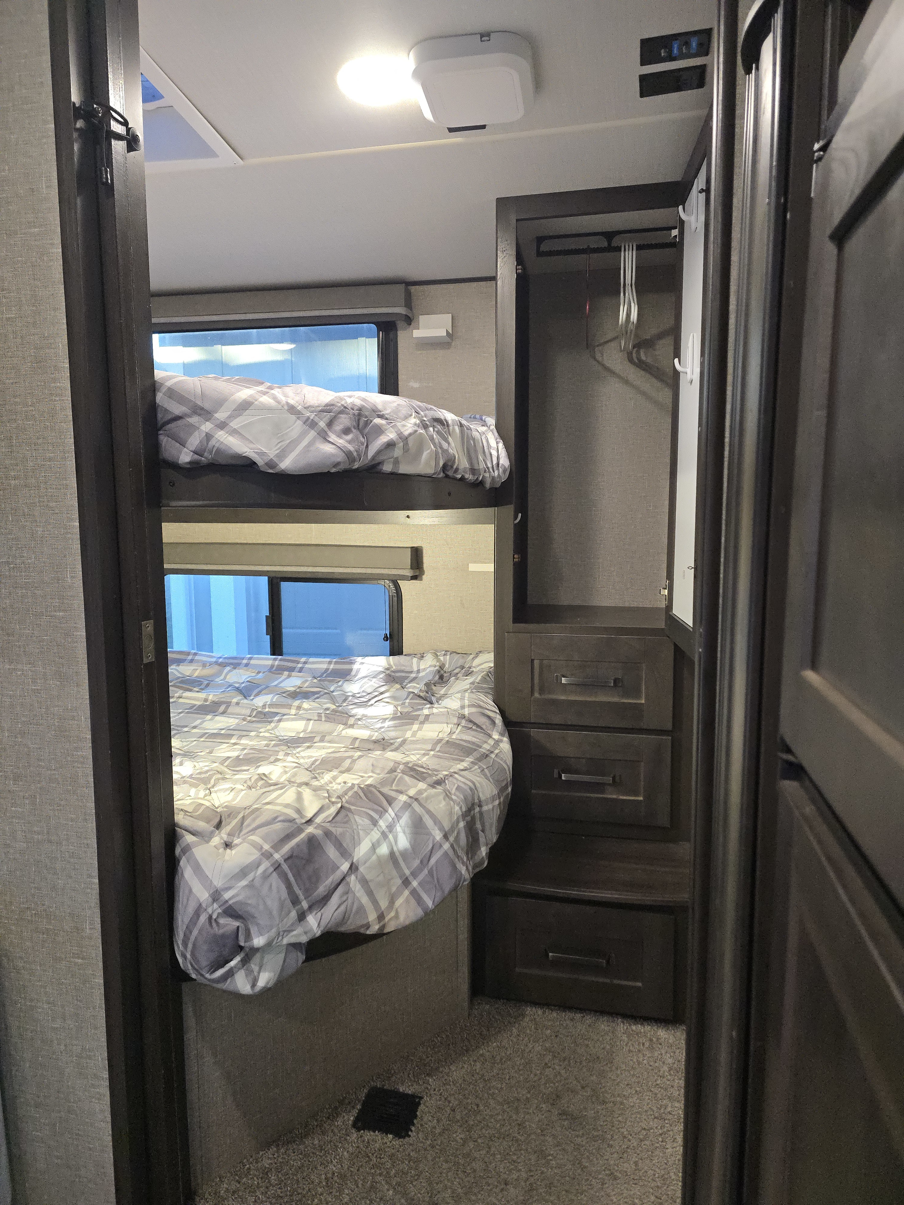 This rv rental bunk bed area features a compact sleeping space with plaid bedding, side windows, and a built-in wardrobe.. Grand Design Reflection 2021