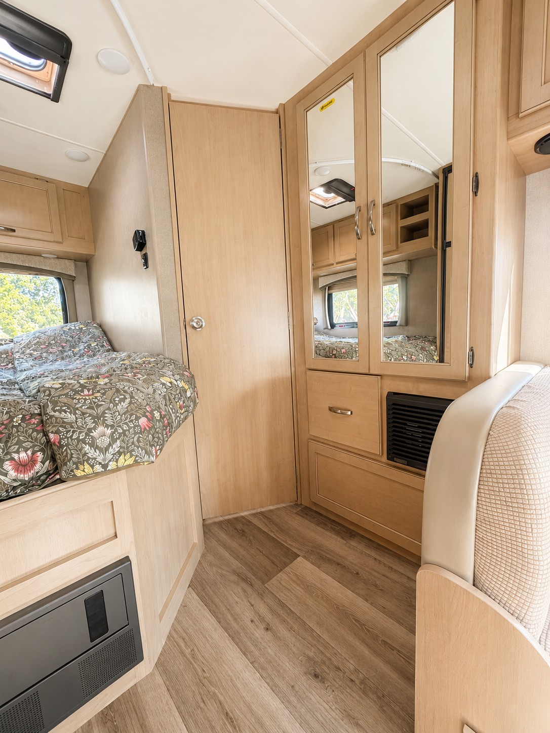Cozy RV rental interior: bedroom with floral bedding, wood-toned cabinets, mirrored wardrobe, and compact living space.. Thor Four Winds 2021