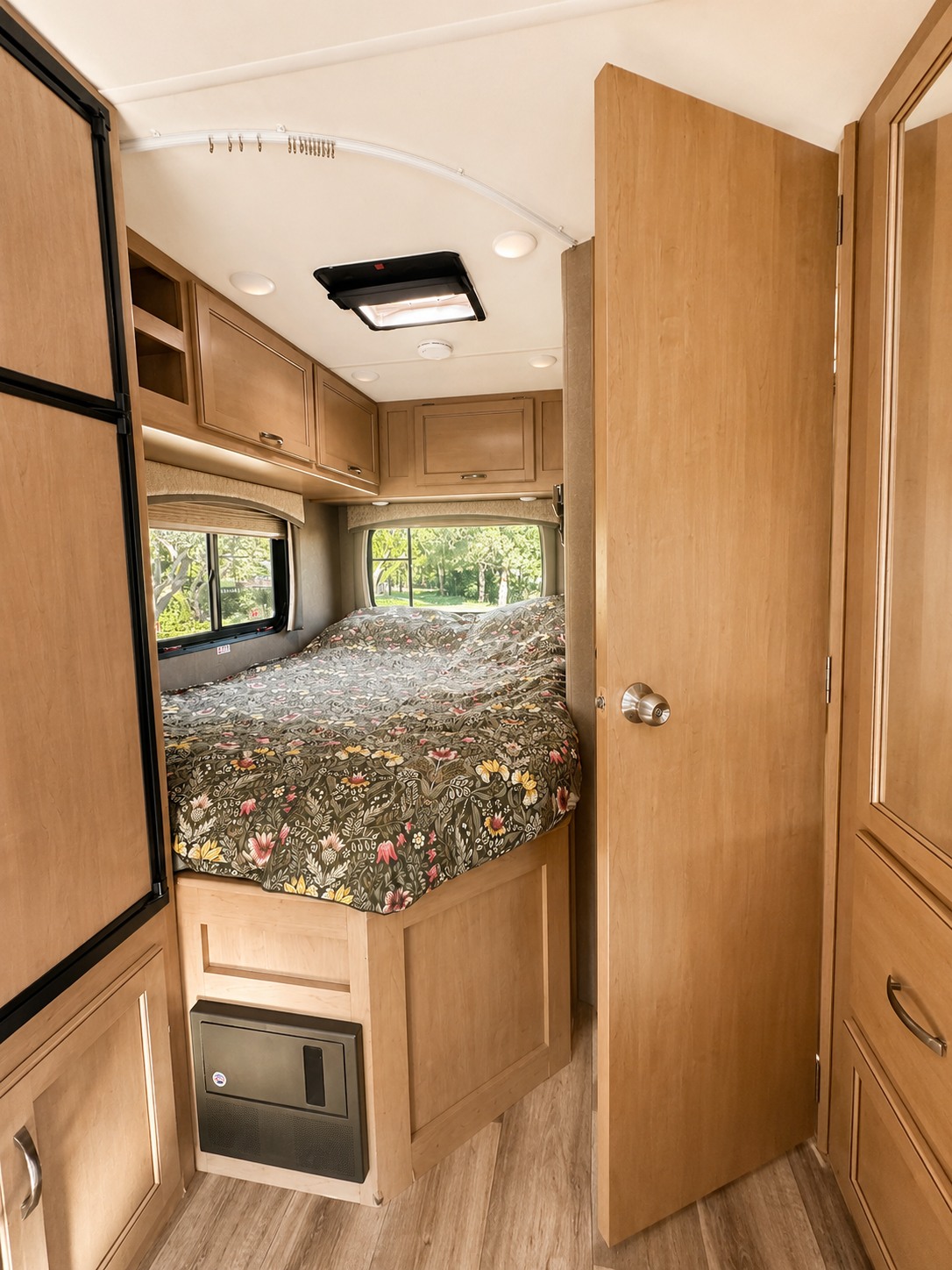 Step inside this inviting RV rental bedroom featuring a floral bed, overhead storage, and adjacent living space for comfortable touring.. Thor Four Winds 2021