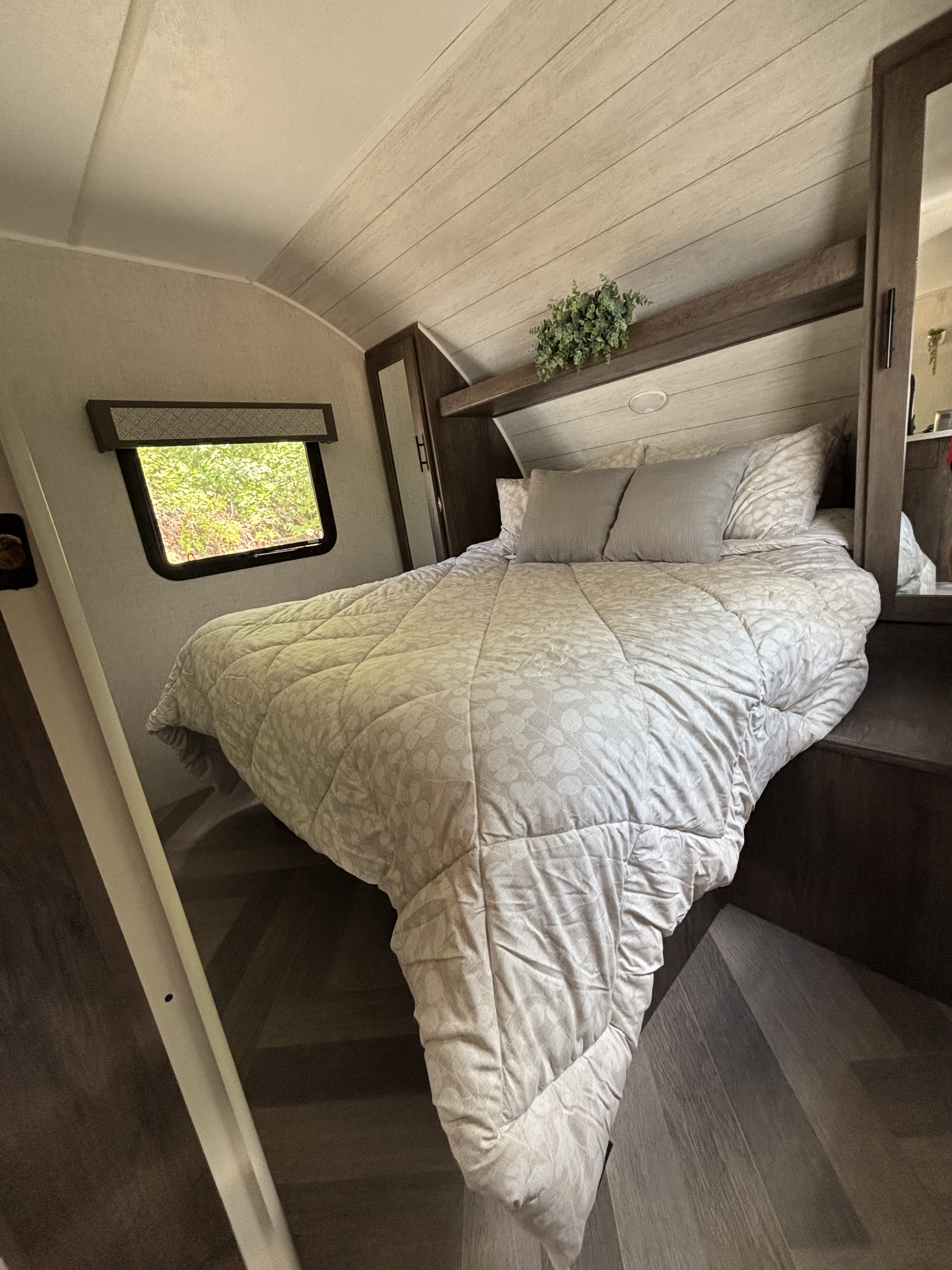 Cozy RV rental bedroom interior, featuring a comfortable bed with patterned comforter, window, and decorative plant.. Forest River Wildwood 2020