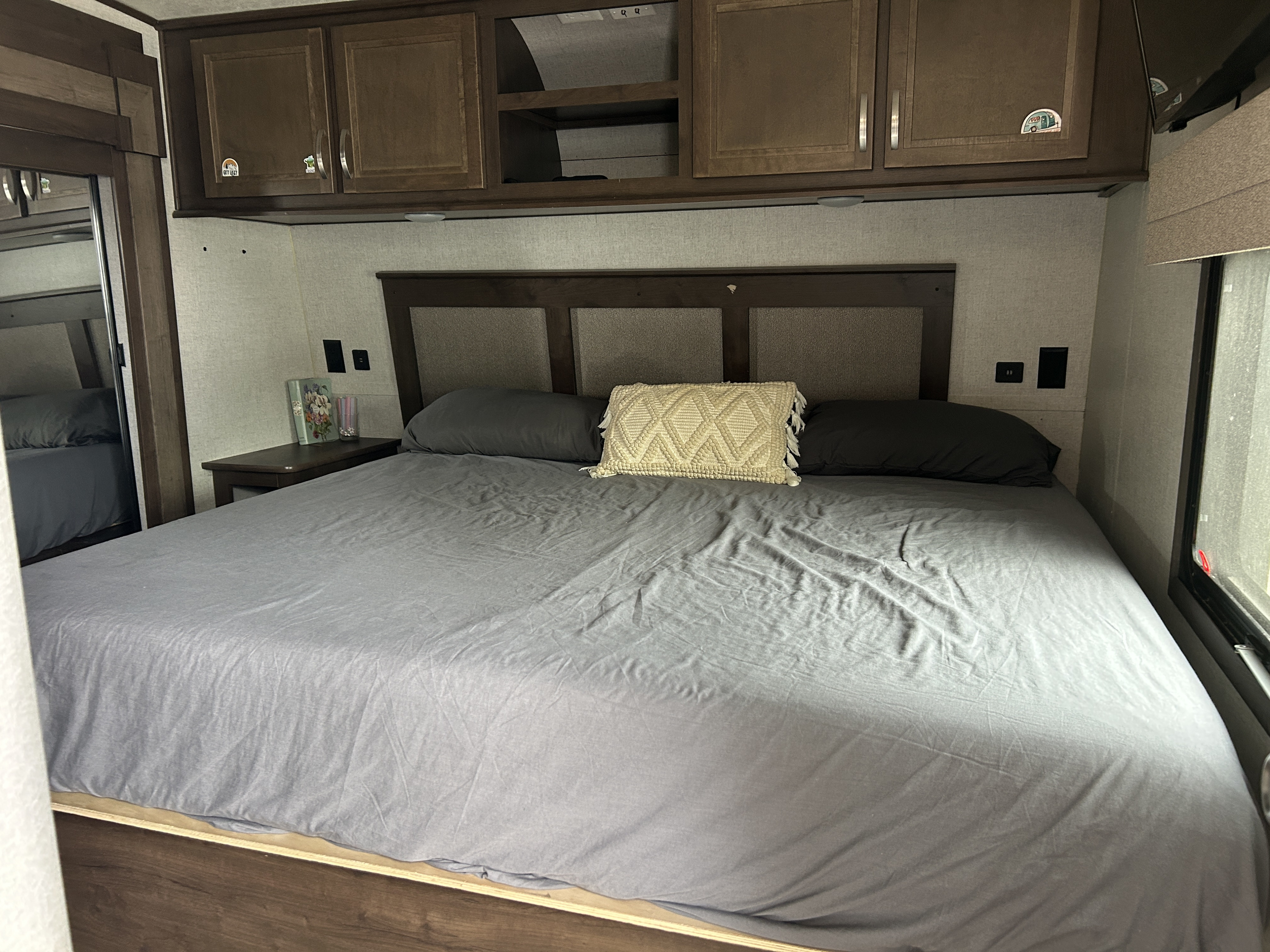 Spacious RV rental bedroom featuring a large bed with grey linens, overhead cabinets, and a stylish headboard.. Highland Ridge RV Open Range 2020