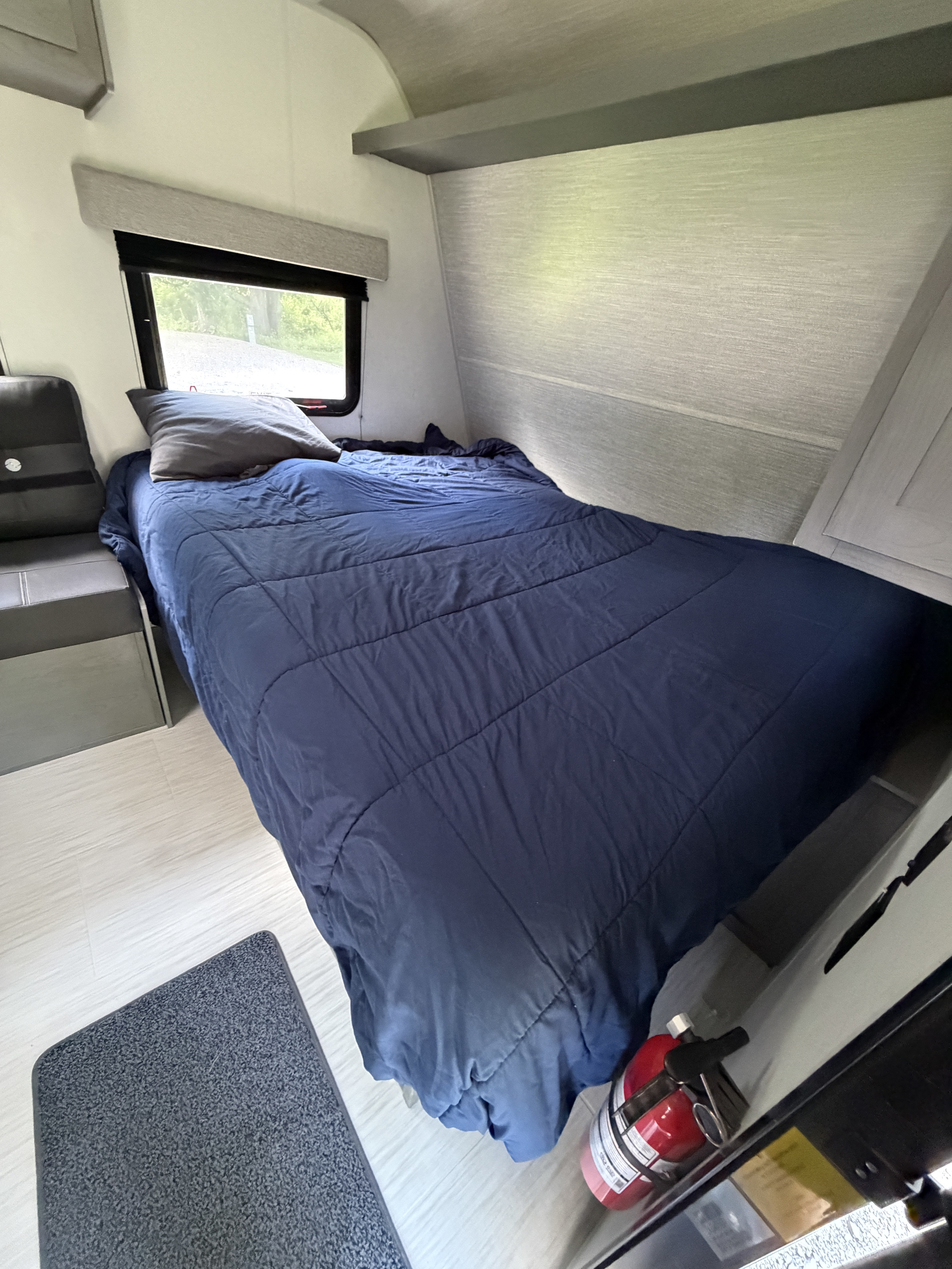 This RV rental features a comfortable, compact bedroom with a navy bed, window, and nearby fire extinguisher.. Ozark Ozark Trailer 2025