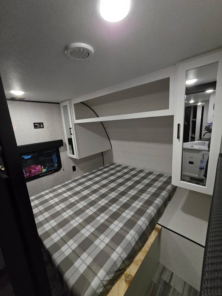Cozy RV rental bedroom with a plaid bed, overhead storage, and window. Perfect for your next adventure.. Jayco Jay Flight SLX 2025