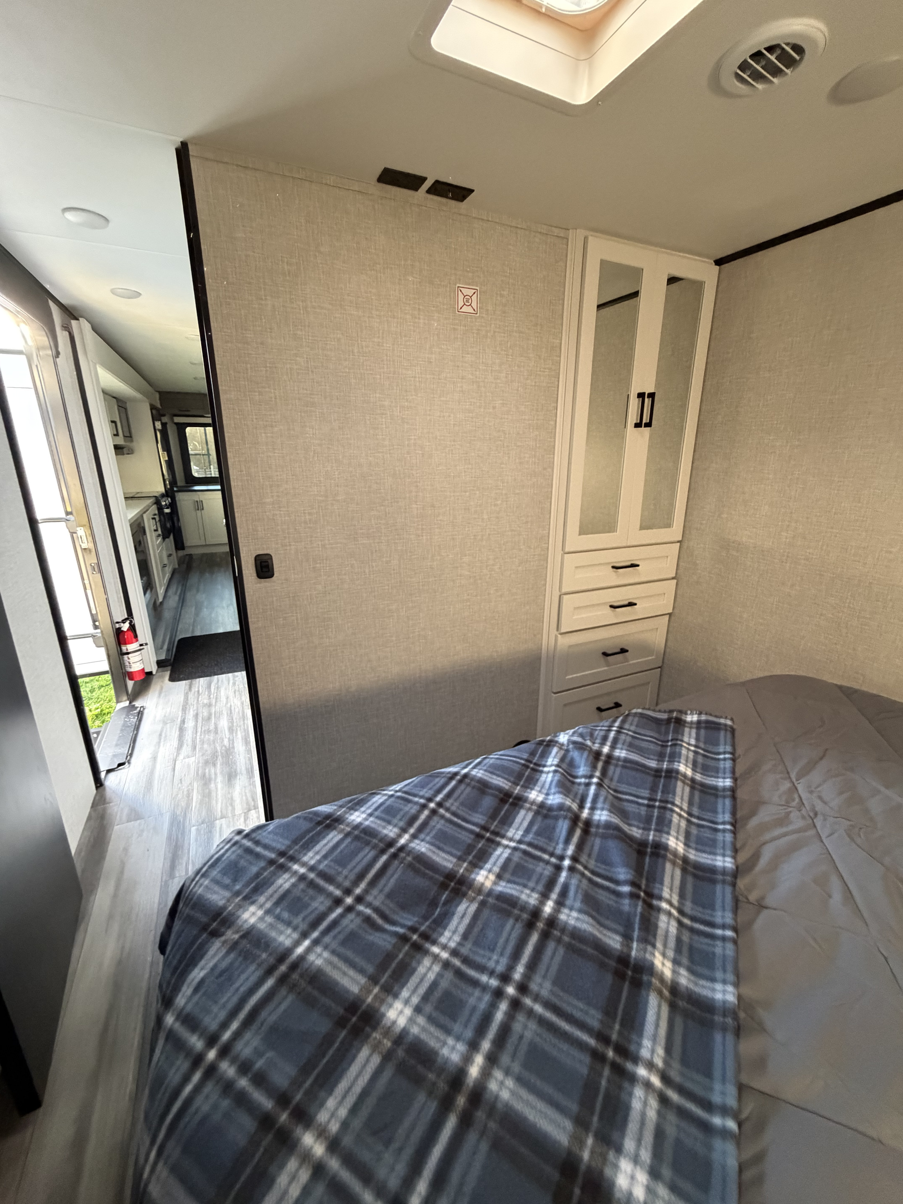 Cozy RV rental bedroom featuring a blue plaid blanket, built-in cabinet with drawers, and an open view to the mobile living space.. Jayco Eagle HT 2025