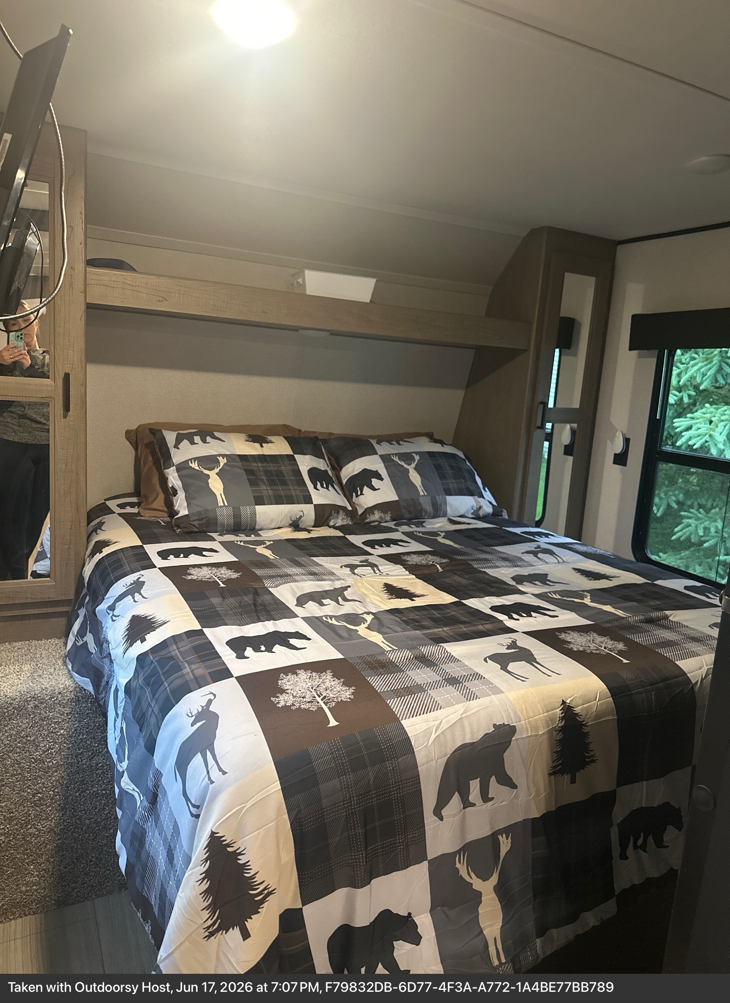 Cozy RV rental bedroom with a rustic quilt featuring bears, deer, and trees; a window shows greenery outside.. Keystone RV Hideout Luxury 2021