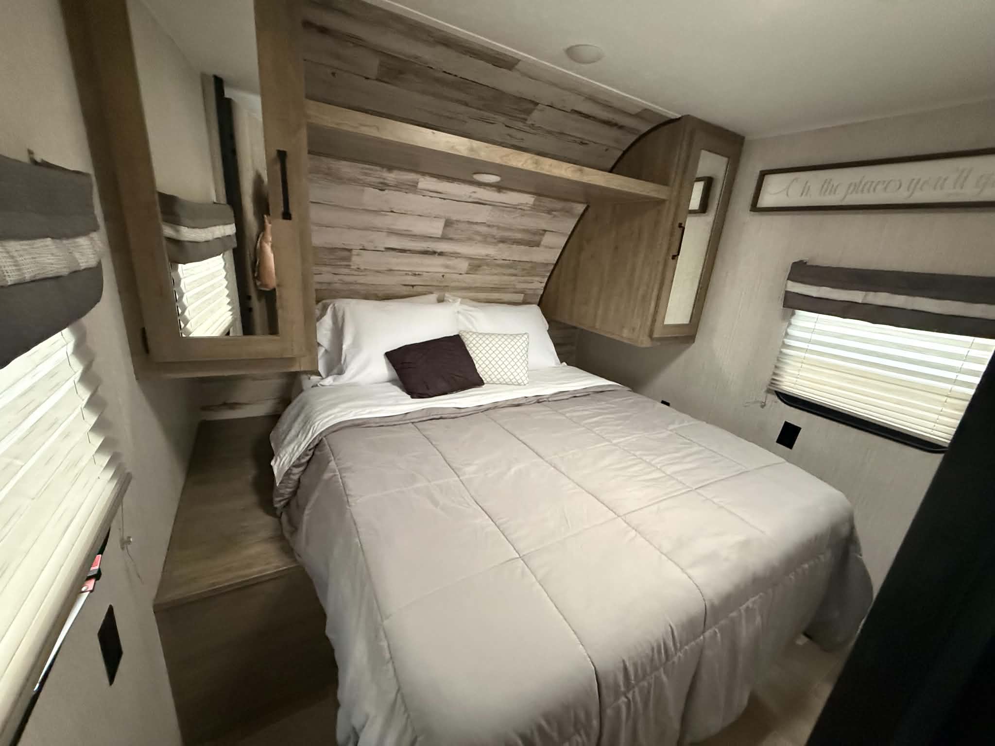 Cozy RV rental bedroom with a queen bed, grey comforter, wood headboard, and built-in mirrored cabinets for a comfortable stay.. Forest River Palomino Puma XLE Lite 2021