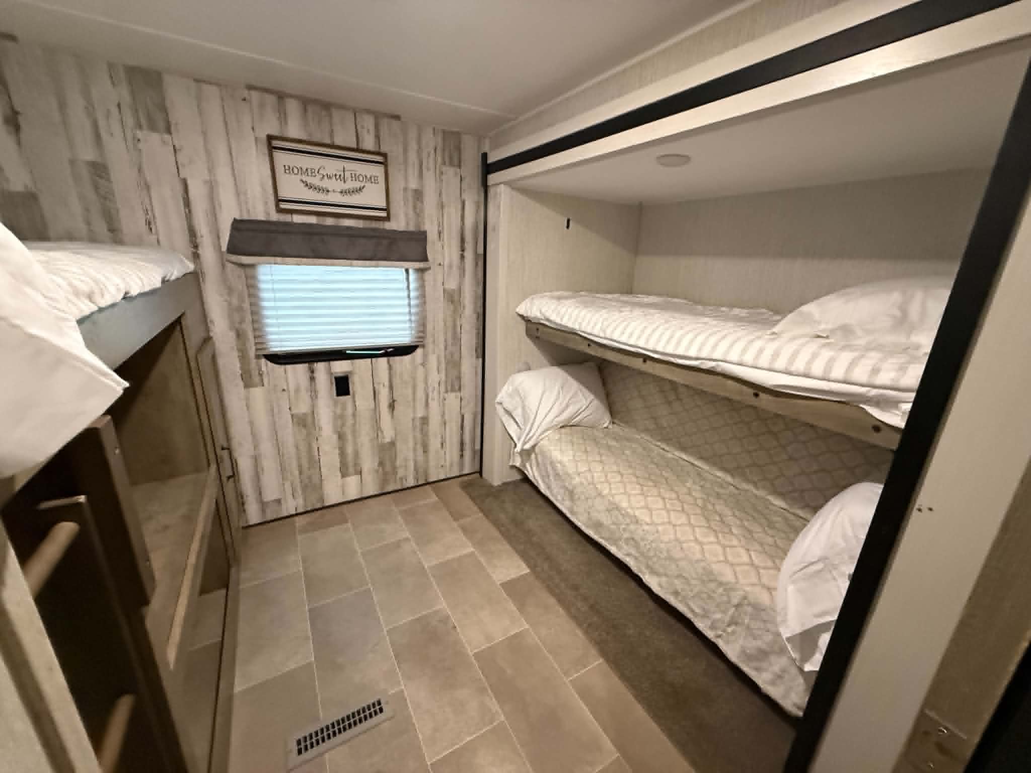 Charming RV rental bunk room with stacked beds, rustic walls, and a window, offering ample sleeping for guests.. Forest River Palomino Puma XLE Lite 2021