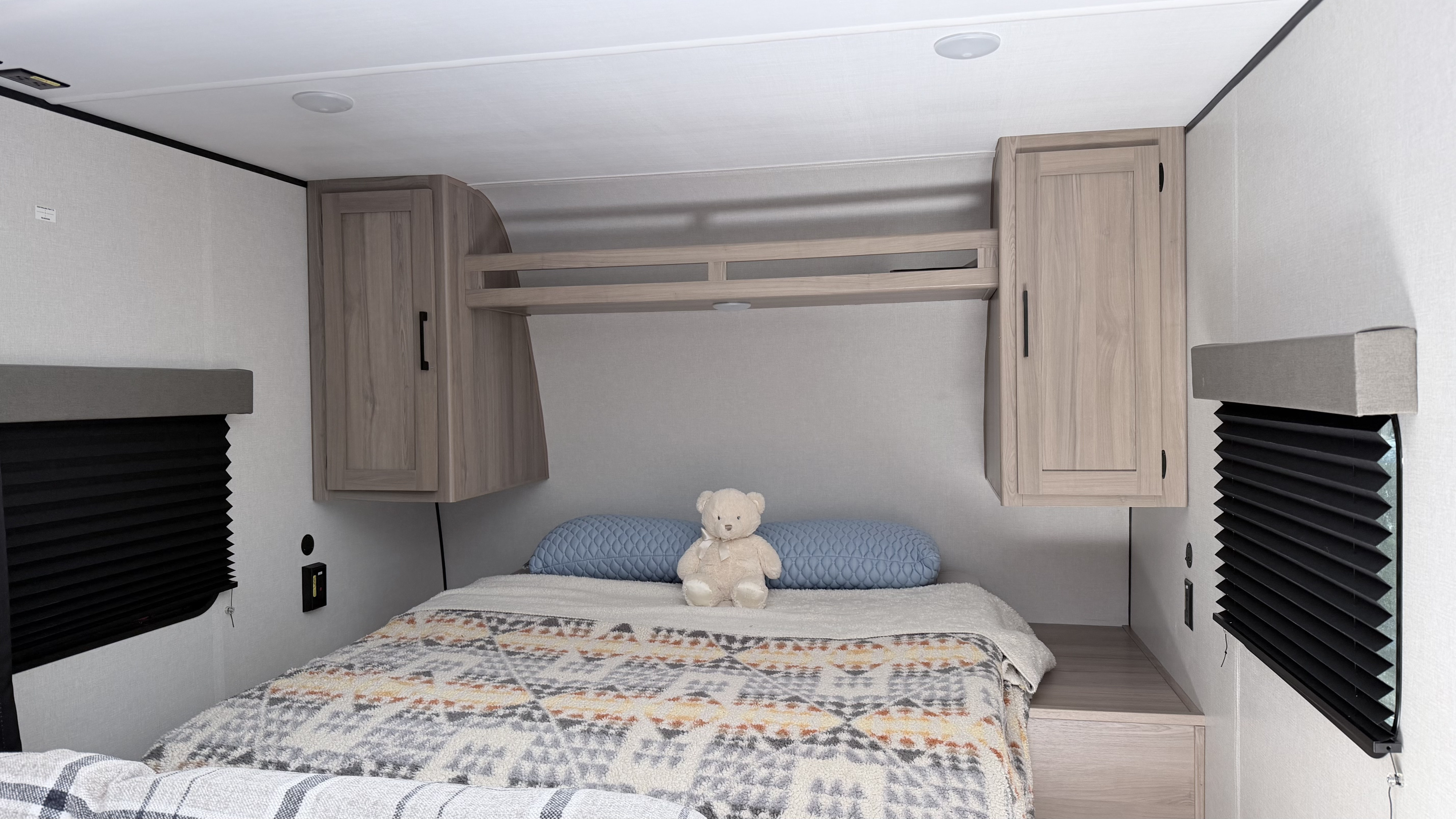An inviting RV rental bedroom with a comfy bed, decorative blankets, a teddy bear, overhead storage, and window blinds.. Keystone RV 23BWE 2026