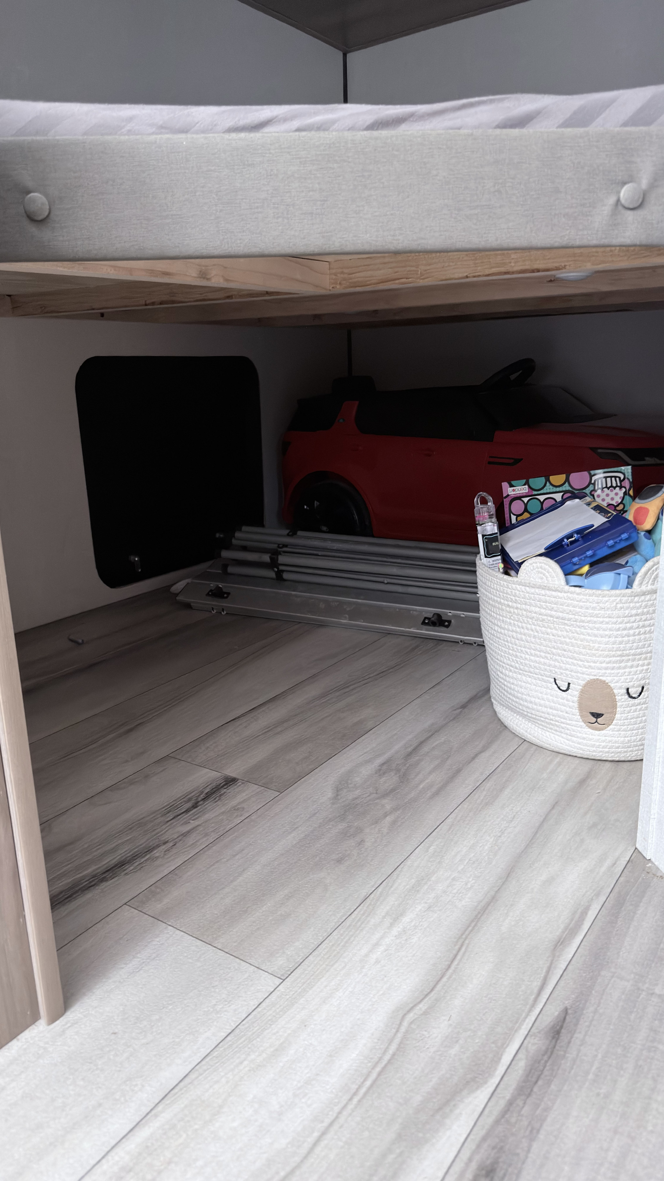RV rental storage: under-bed space with a red toy car, folded items, and a cute basket of kids' toys on wood flooring.. Keystone RV 23BWE 2026