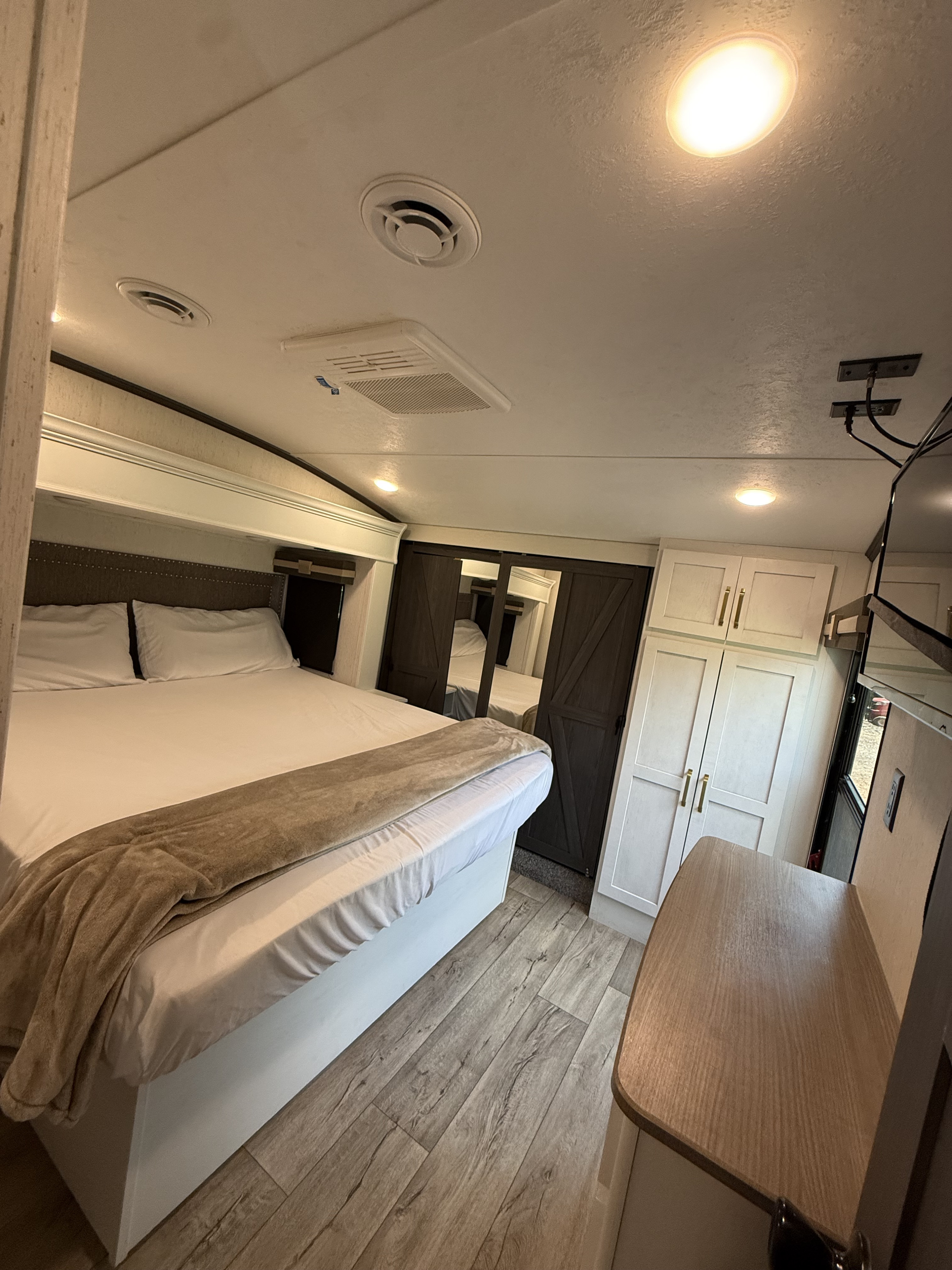This bright RV rental bedroom features a comfy bed with white linens, stylish light cabinets, dark barn doors, and wood-look flooring.. Astoria Platinum 2022