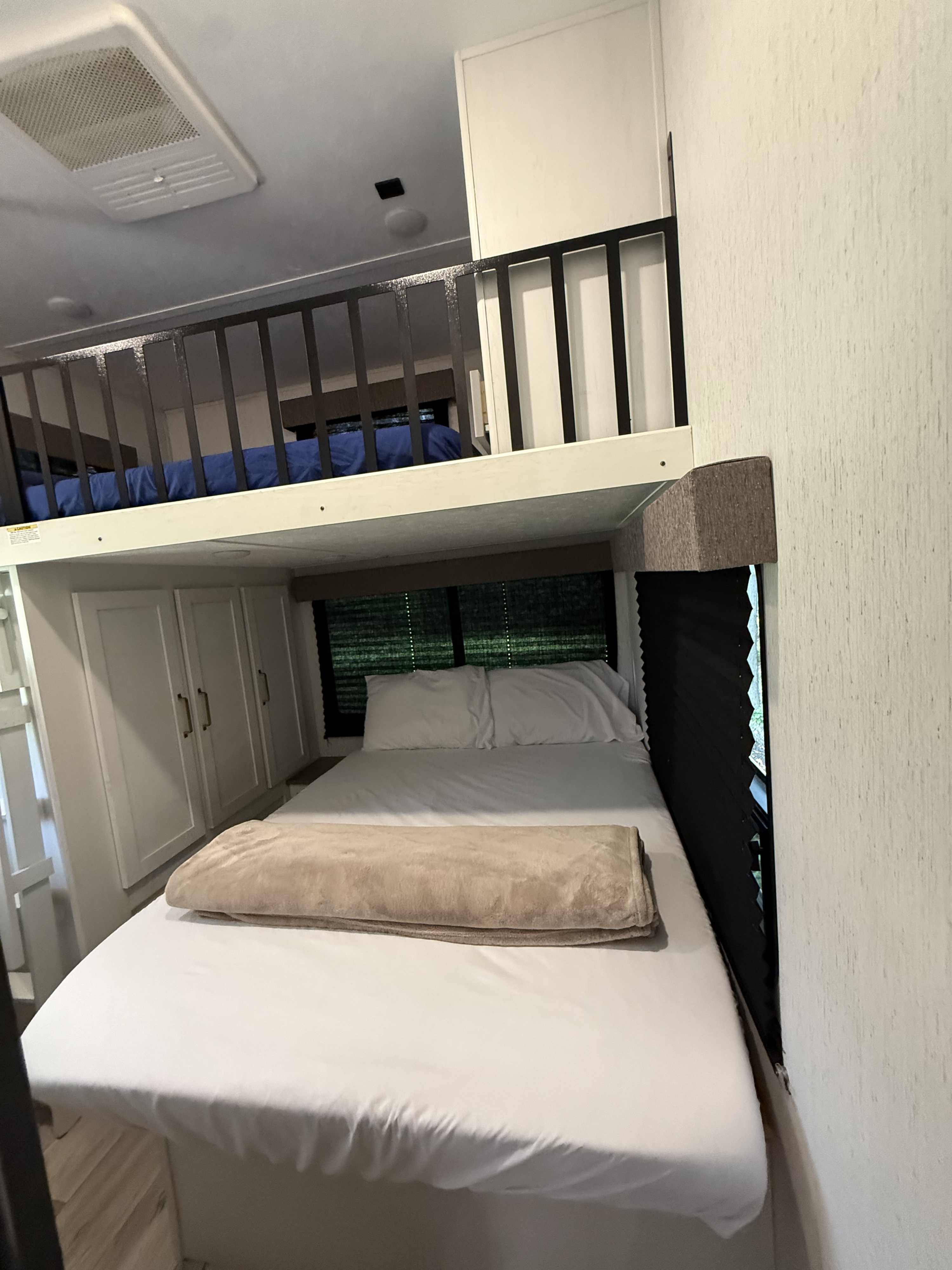 Cozy rv rental bedroom features a main bed with white linens & blanket, plus a charming loft bed above with a security railing.. Astoria Platinum 2022