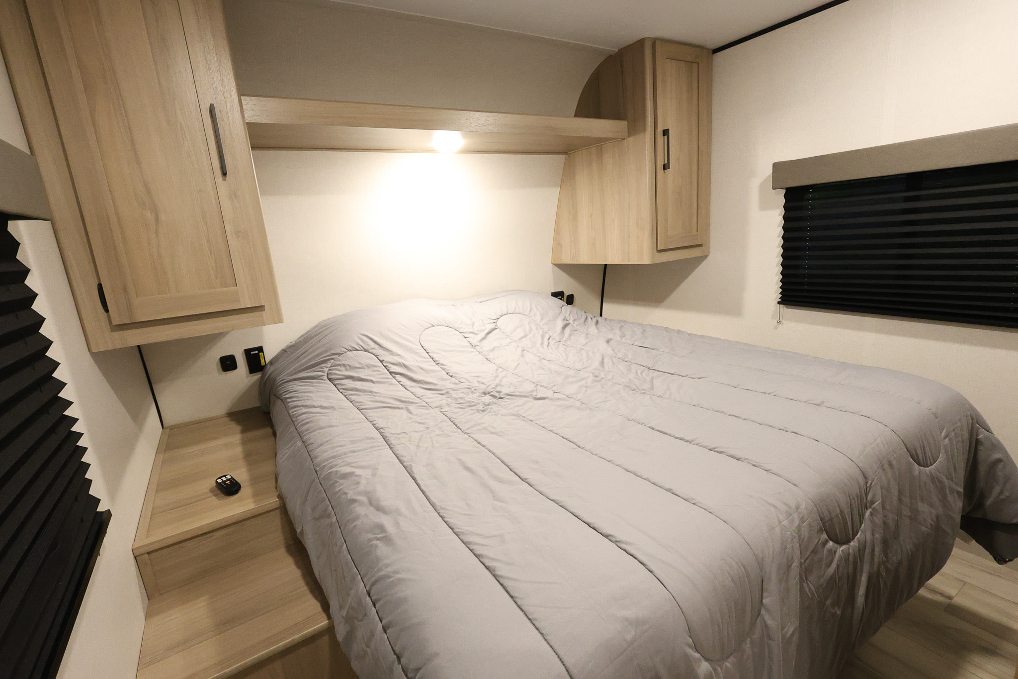 Cozy RV rental bedroom with a grey bed, overhead cabinets, and compact built-in storage. Ideal for travel.. Keystone RV Coleman Light 2025