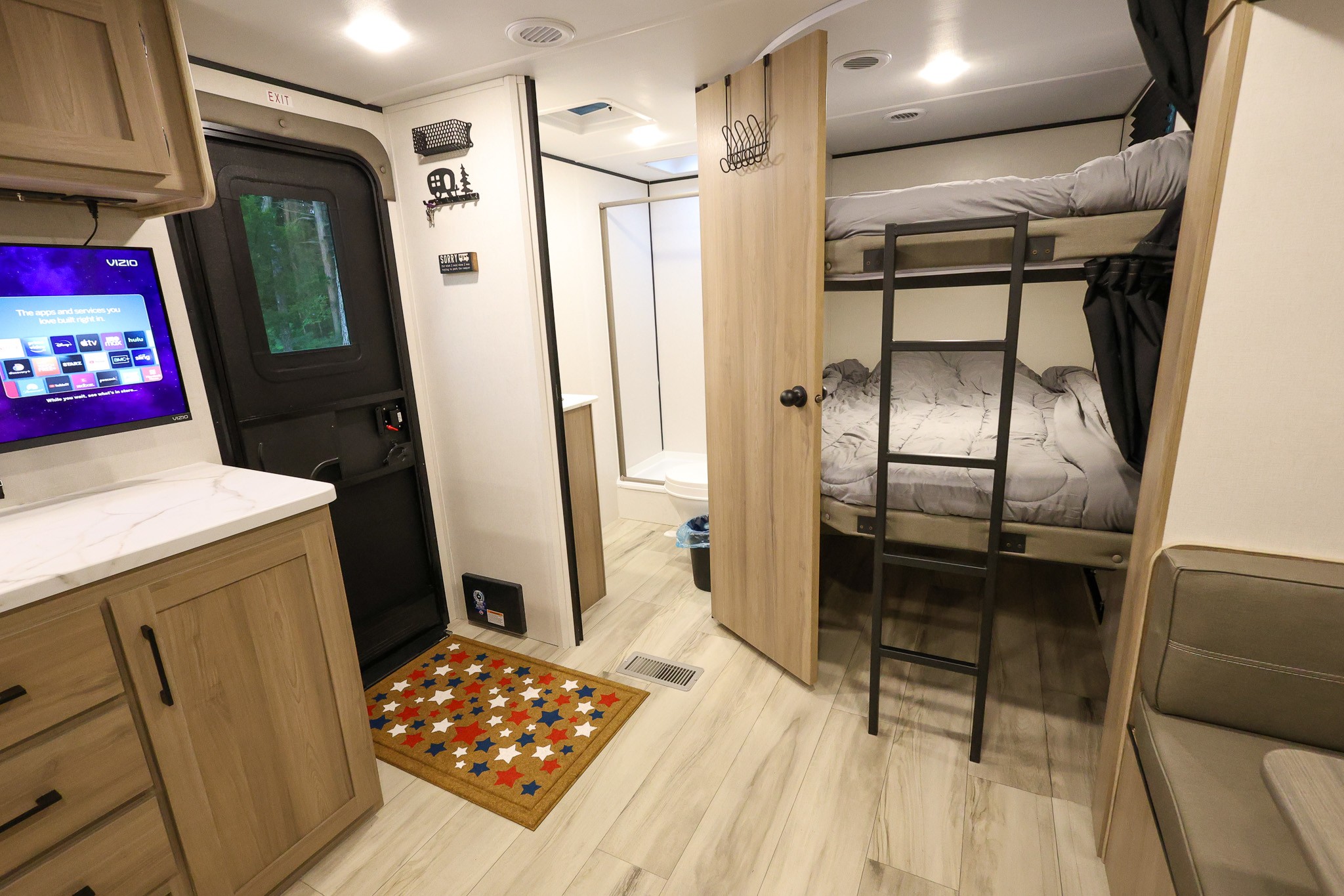 A cozy RV rental interior showing bunk beds, kitchen counter, smart TV, and a glimpse of the bathroom.. Keystone RV Coleman Light 2025