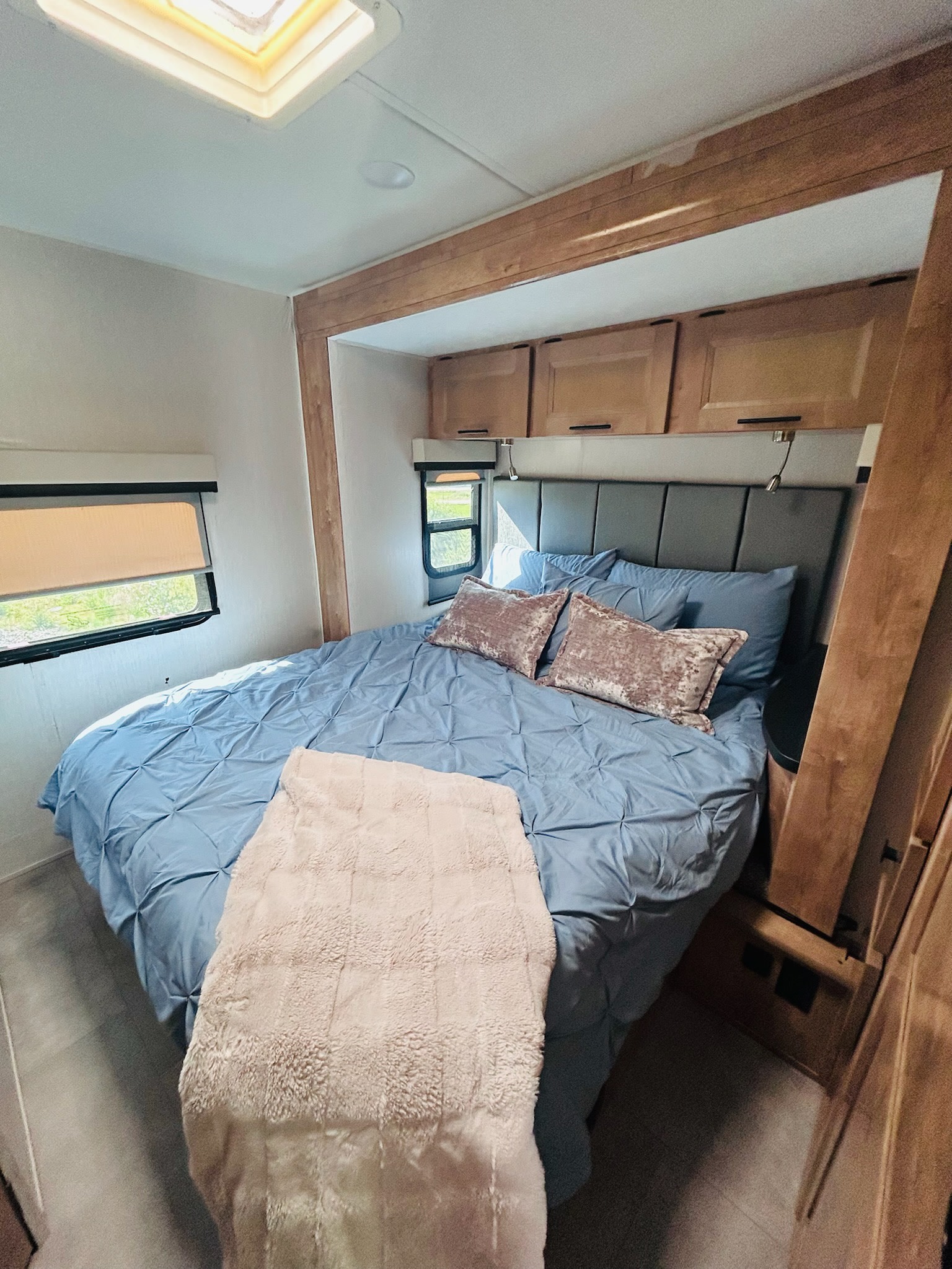 Comfortable RV rental bedroom with blue bed, padded headboard, and overhead cabinets. Natural light from skylight & windows.. Forest River Coachmen Prism Elite 2020