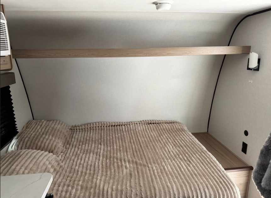 Relax in this cozy RV rental bedroom. Features a comfy bed with beige ribbed blanket, storage shelf, and amenities.. Keystone RV Coleman Legacy 2026