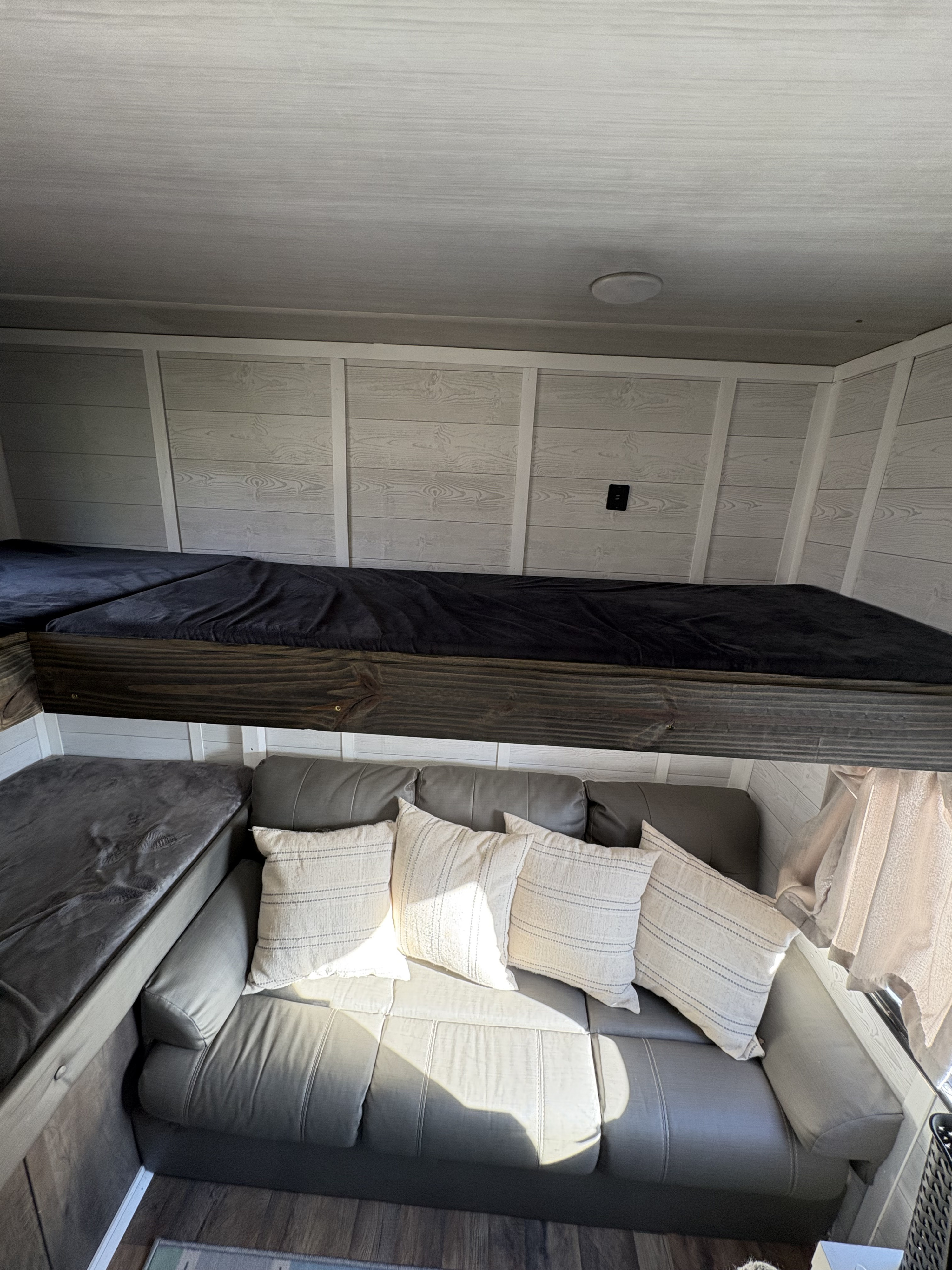 Cozy rv rental interior featuring a bunk bed above a gray couch and secondary seating. Light wood paneling creates a bright living space.. Forest River Salem Cruise Lite 2020